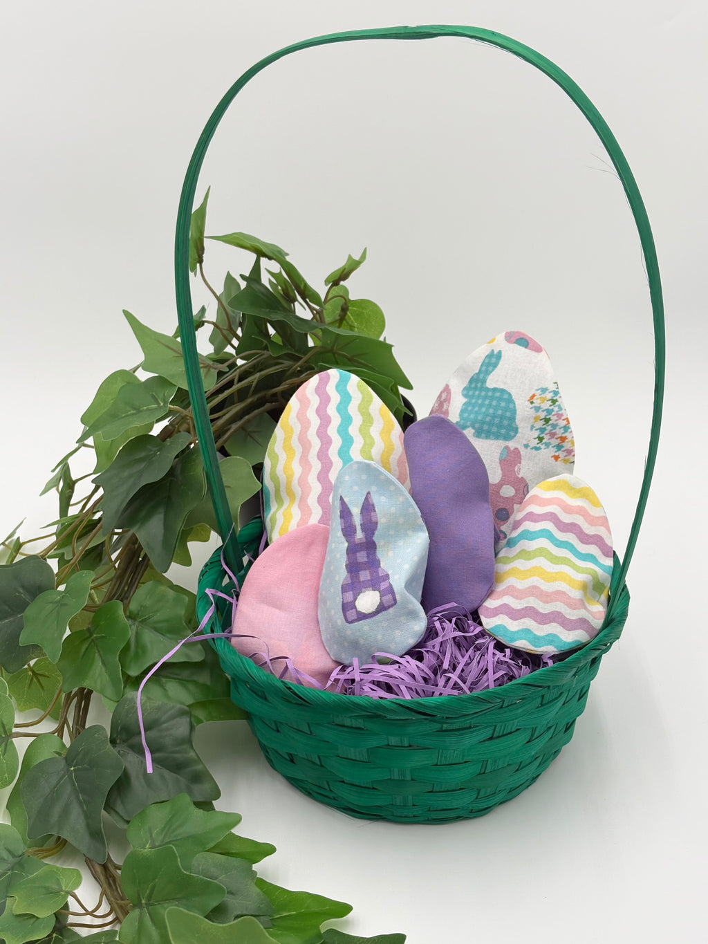 Green Easter basket with Colorful fabric Easter egg fillers on a white background with green leaves.