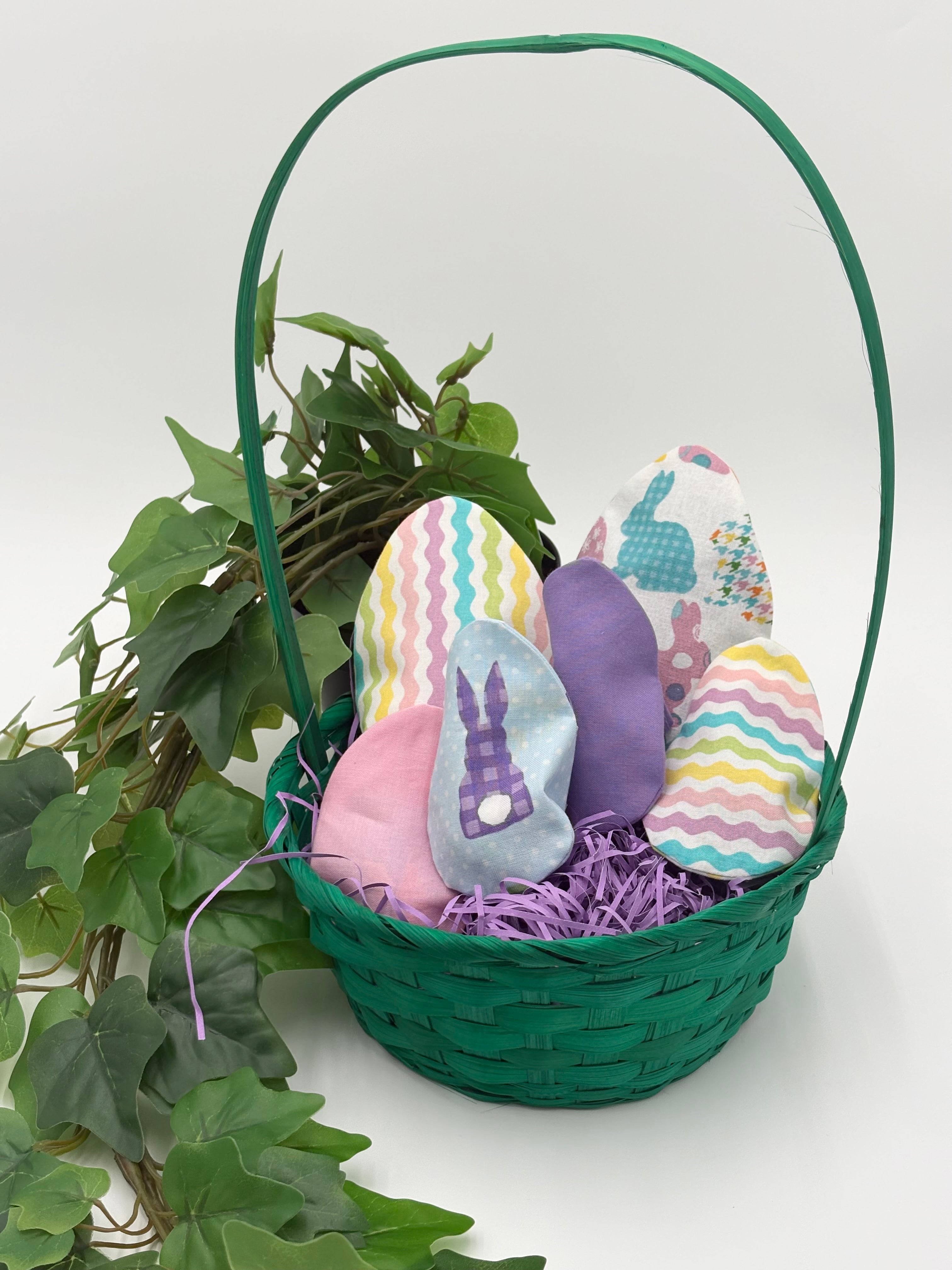 Green Easter basket with Colorful fabric Easter egg fillers on a white background with green leaves.