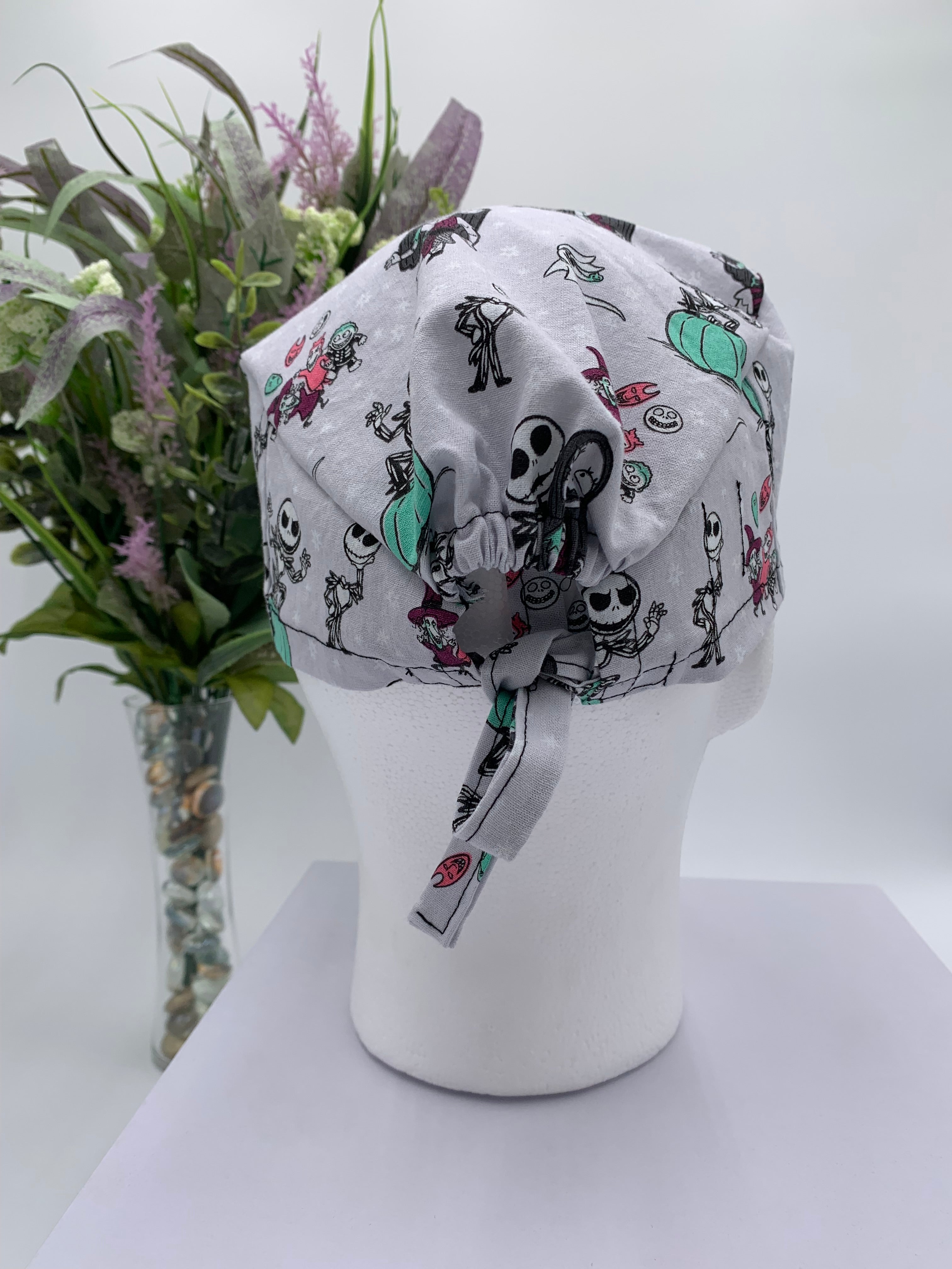 Mannequin head wearing a nightmare before christmas scrub cap with a decorative plant in the background.
