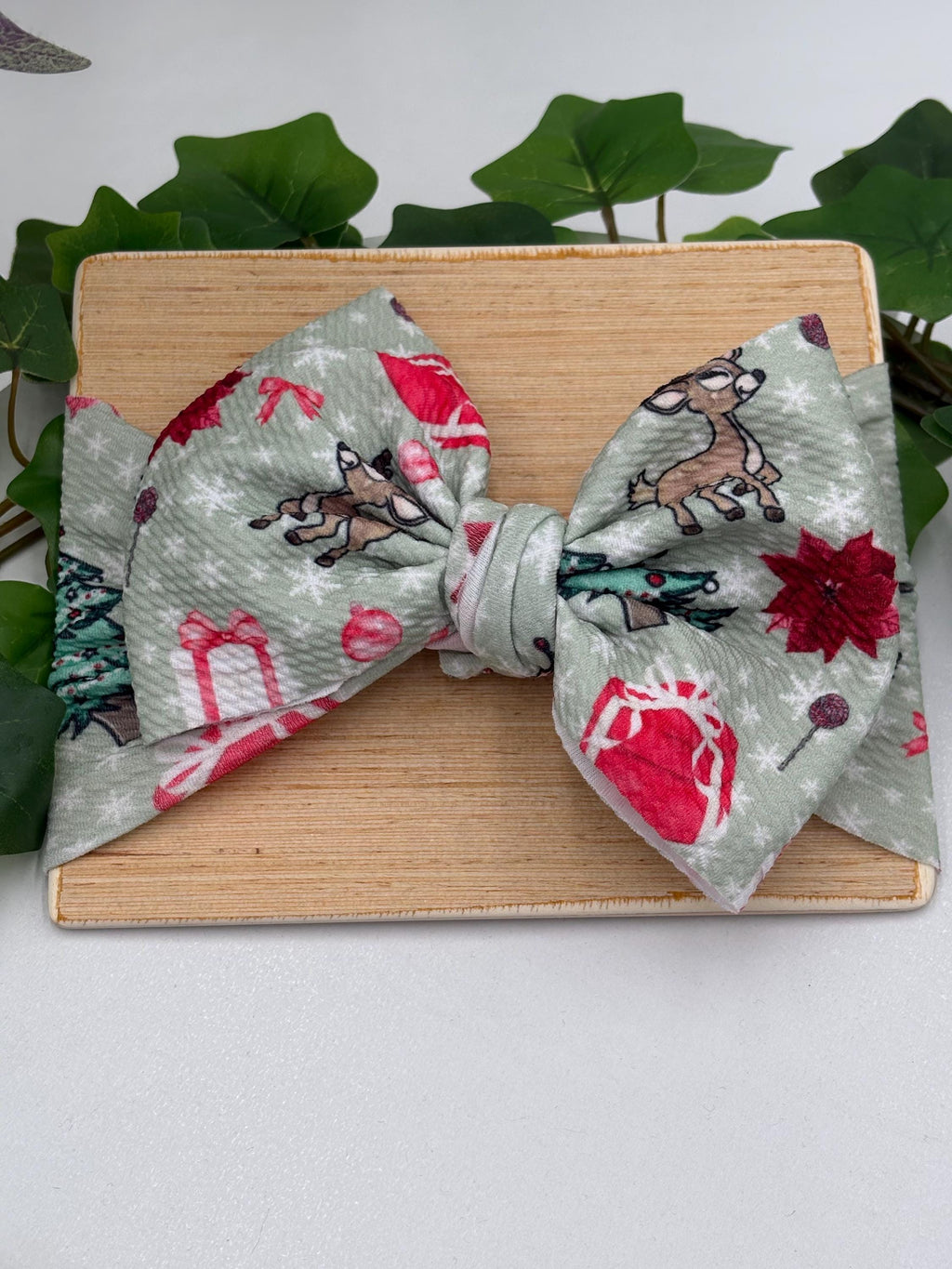 Headband with a decorative christmas themed big bow headband on a wooden plank against a white background