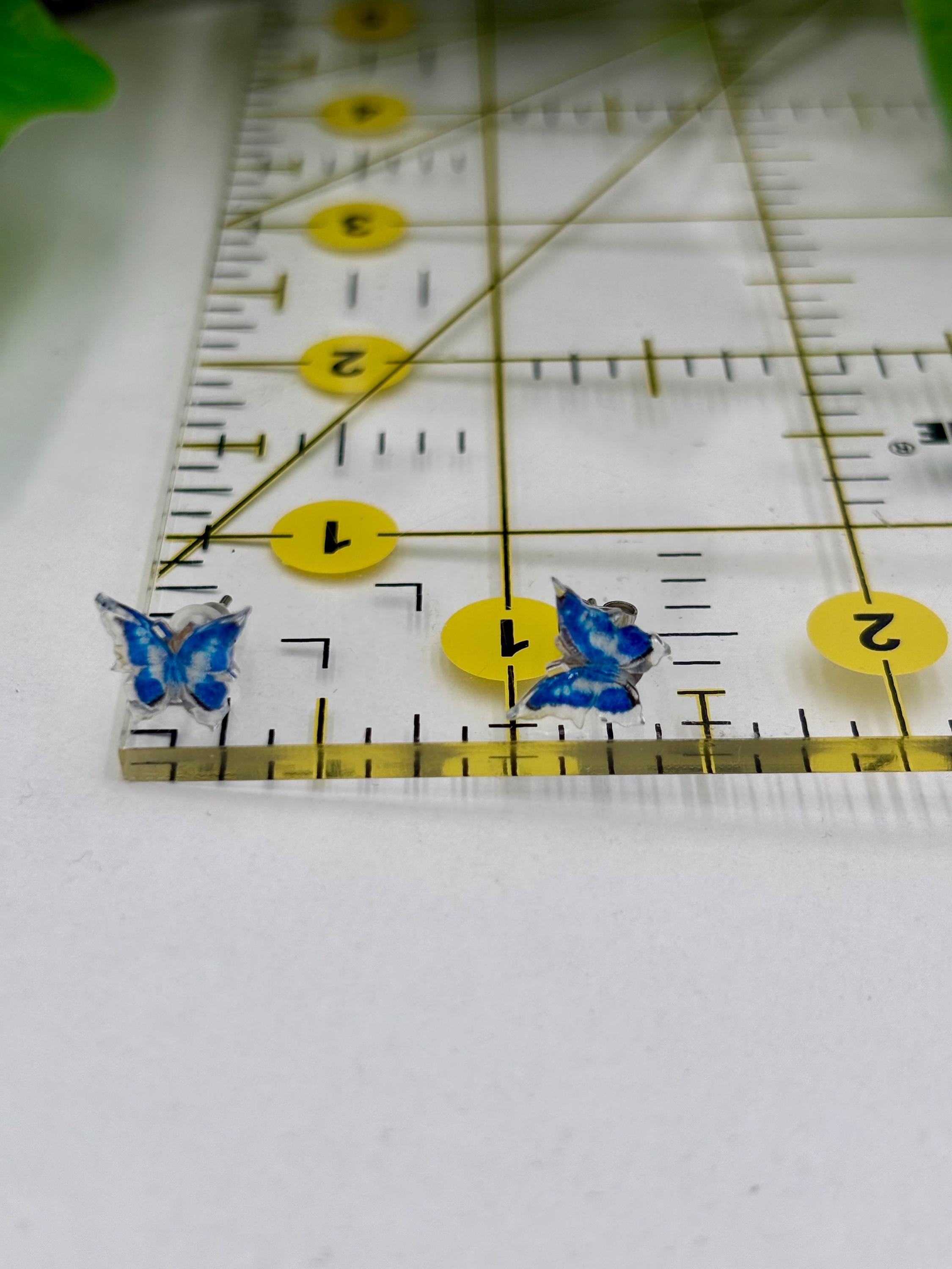 Two blue butterfly earrings on a ruler for scale