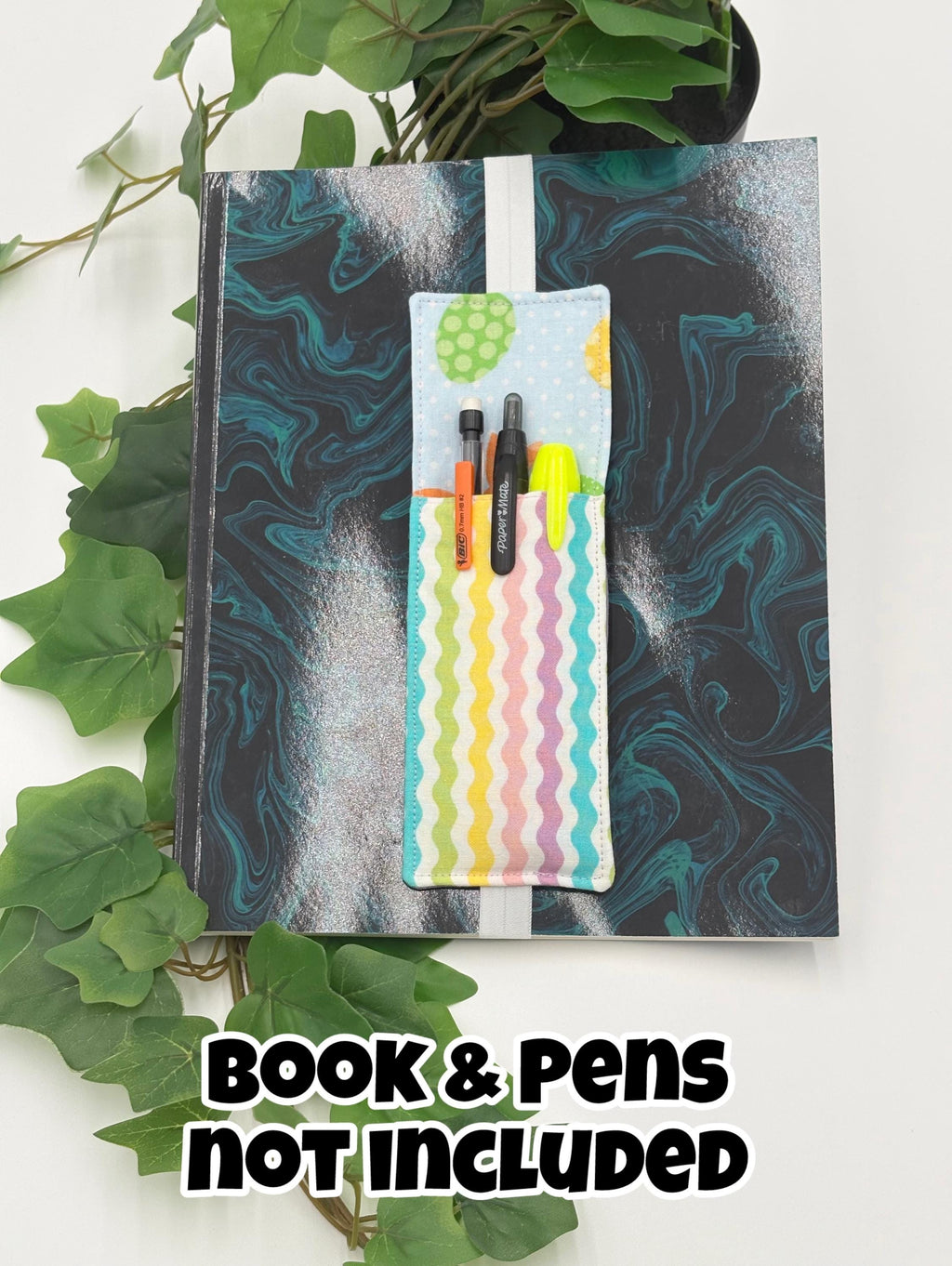 Pastel multi-colored pen holder book mark with easter egg pattern on a marbled black and blue surface, with text 'Book & Pens Not Included'.