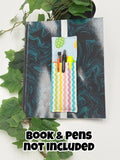 Pastel multi-colored pen holder book mark with easter egg pattern on a marbled black and blue surface, with text 'Book & Pens Not Included'.