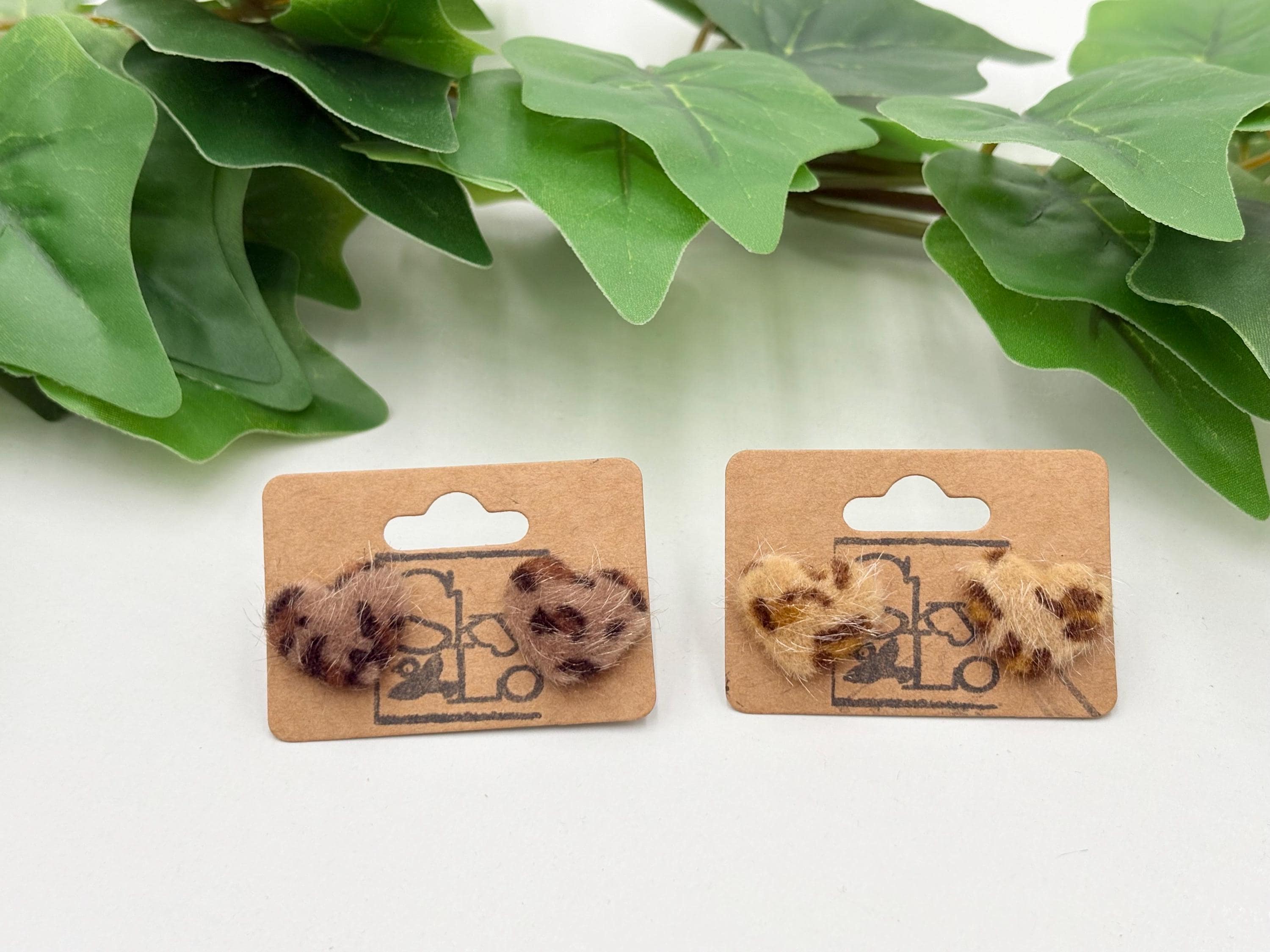 set of two leopard print earrings on wooden display cards with green leaves in the background