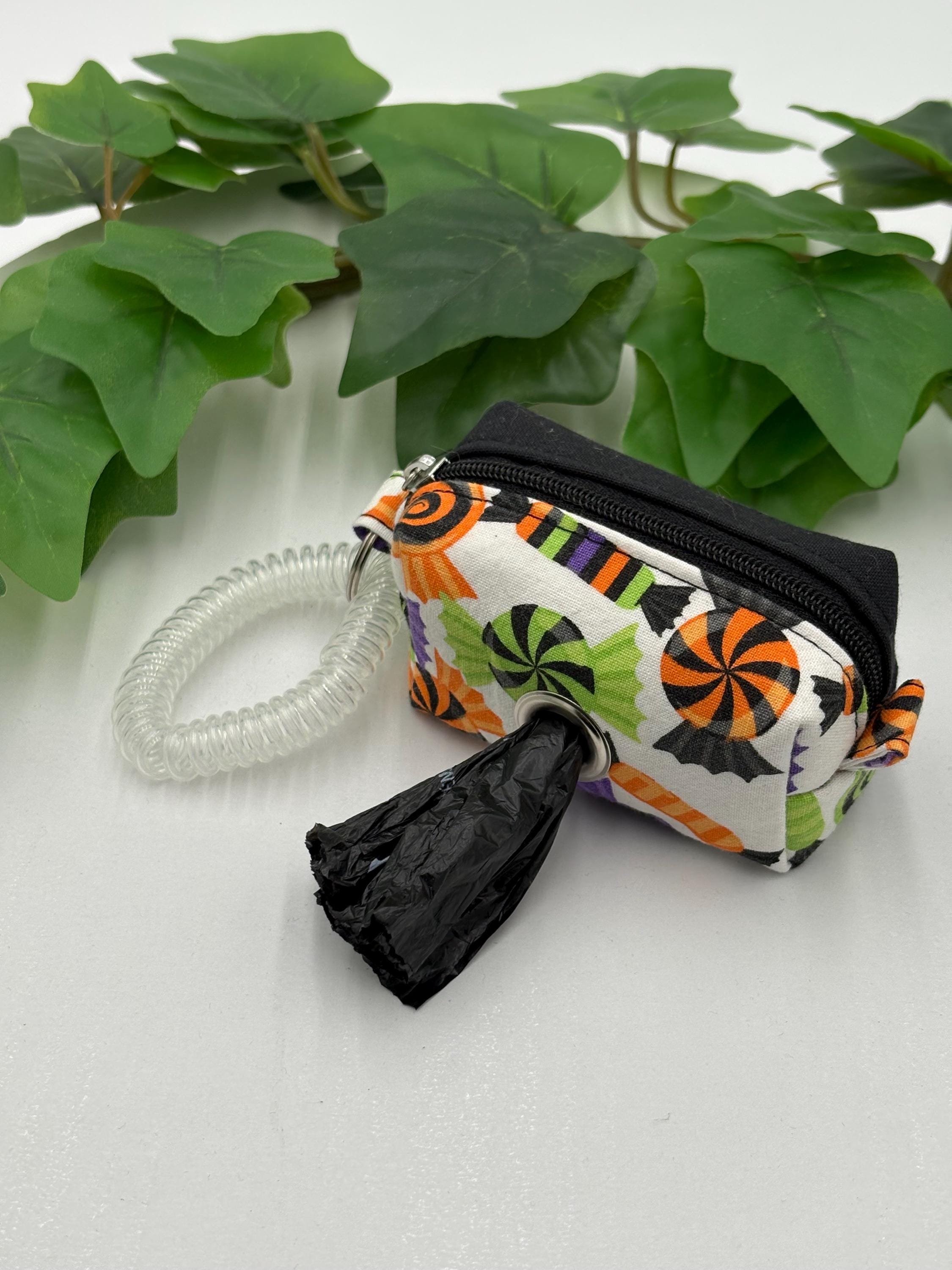 Dog waste bag dispenser with Halloween pattern on a white background with green leaves.