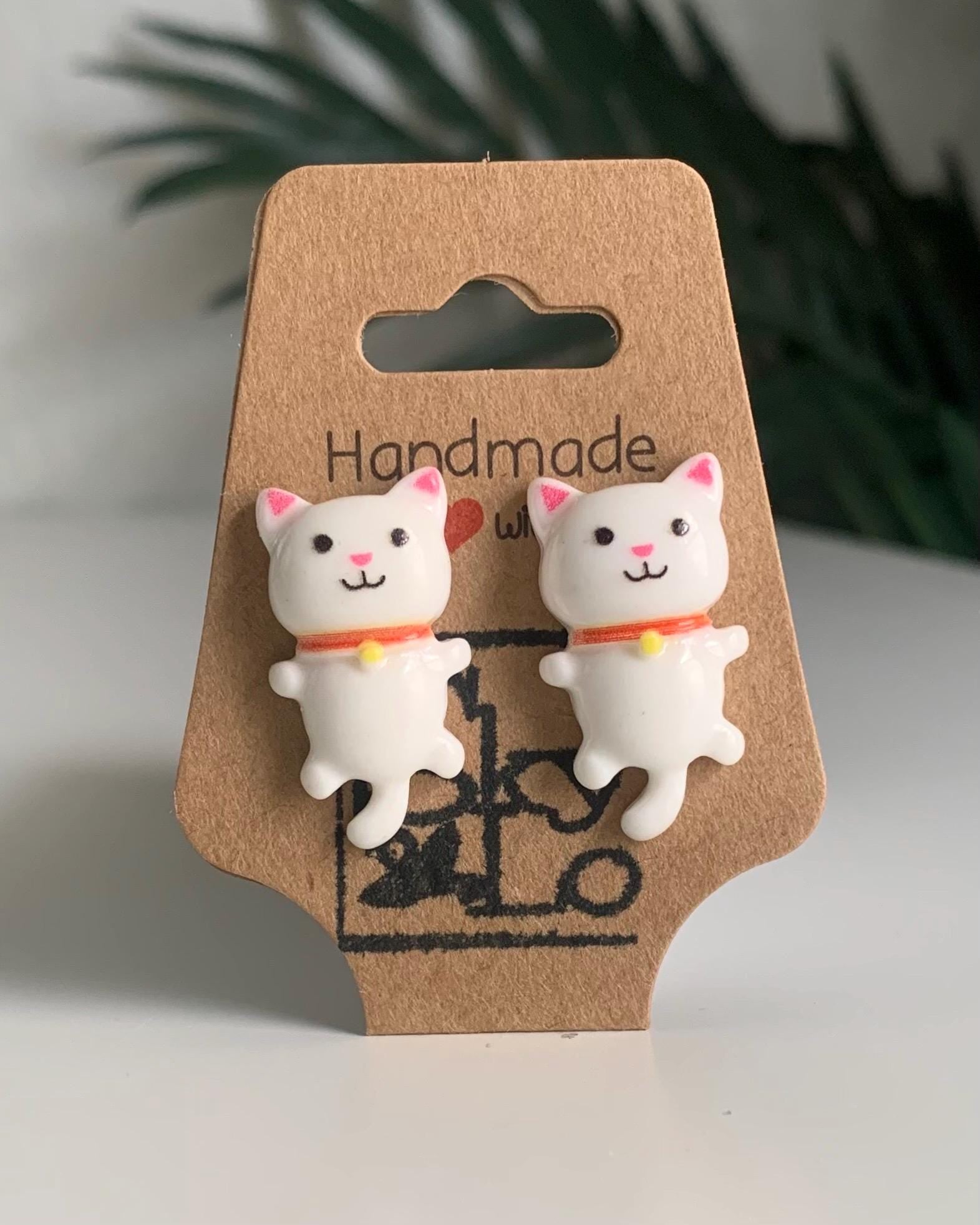 White Cat-shaped earrings on a 'Handmade' card with a plant in the background