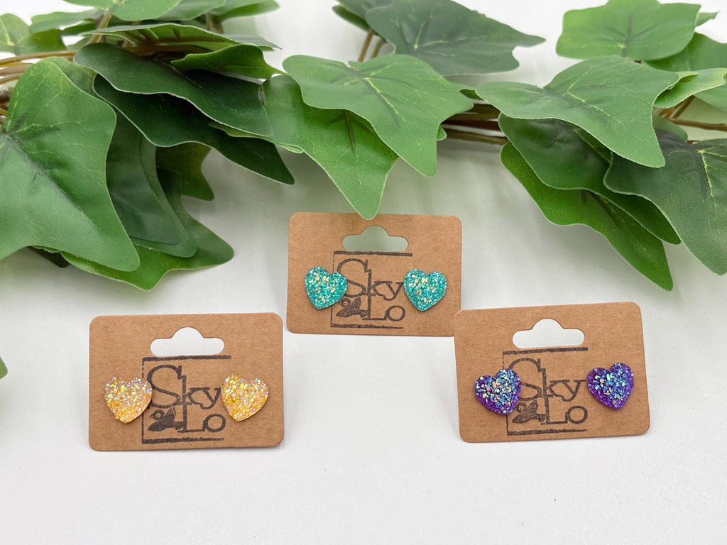 Three sets of sparkling Heart-shaped earrings on display with green leaves in the background