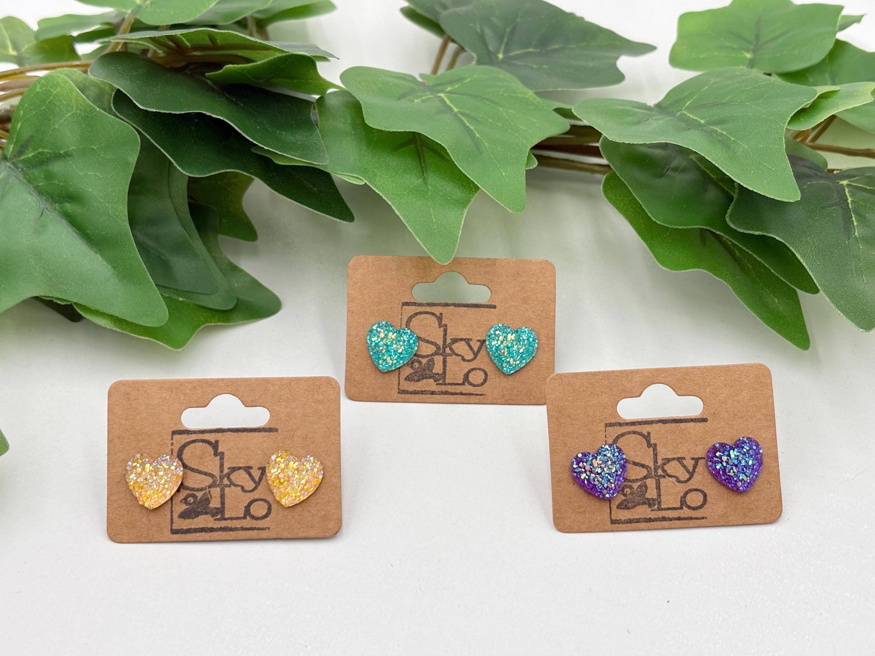 Three sets of sparkling Heart-shaped earrings on display with green leaves in the background