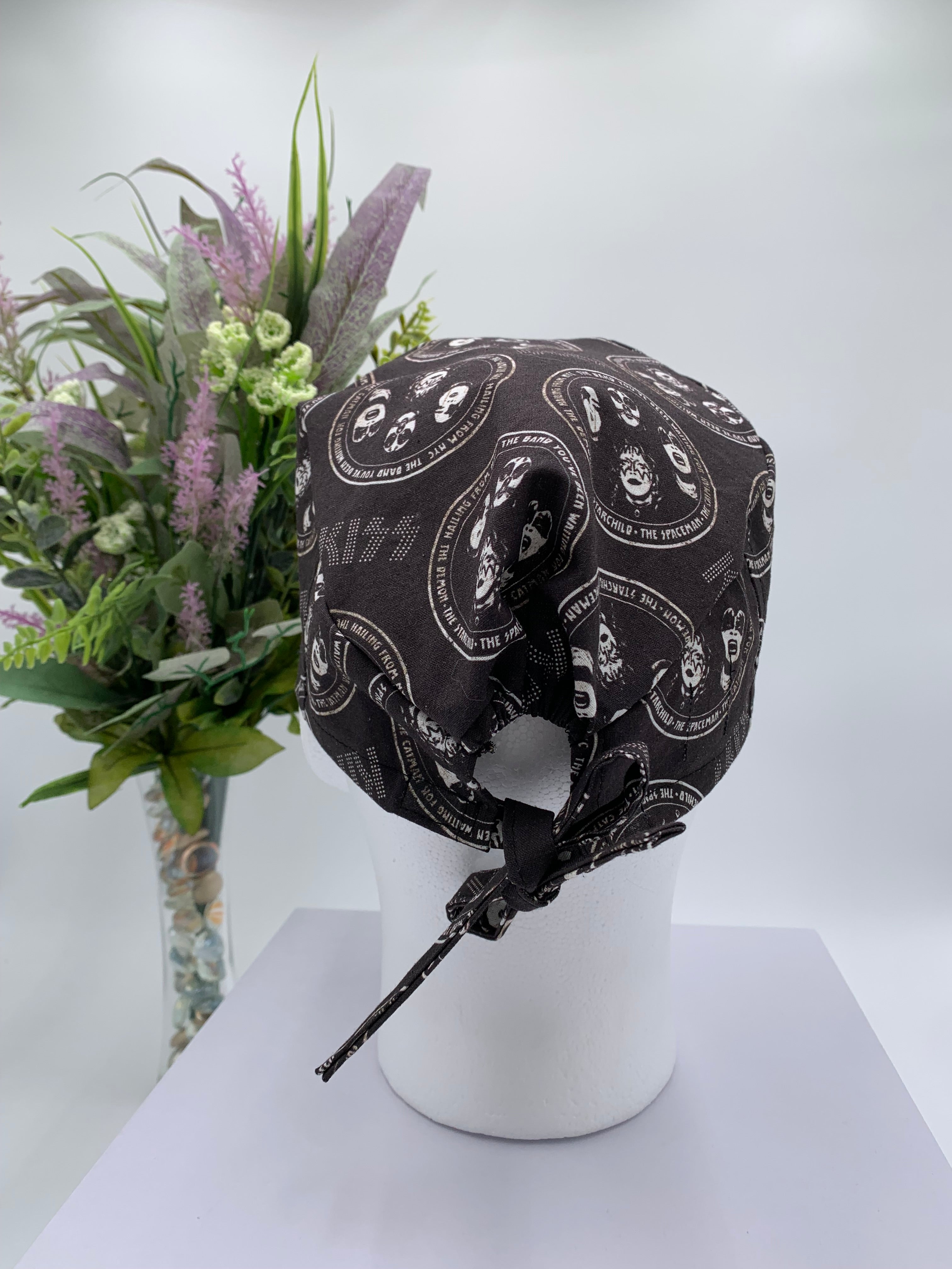 Black KISS band patterned scrub cap on a mannequin head with a white background with flowers