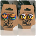 Pair of Mario bros fire flower and question block earrings on a 'Handmade' branded card with a logo.