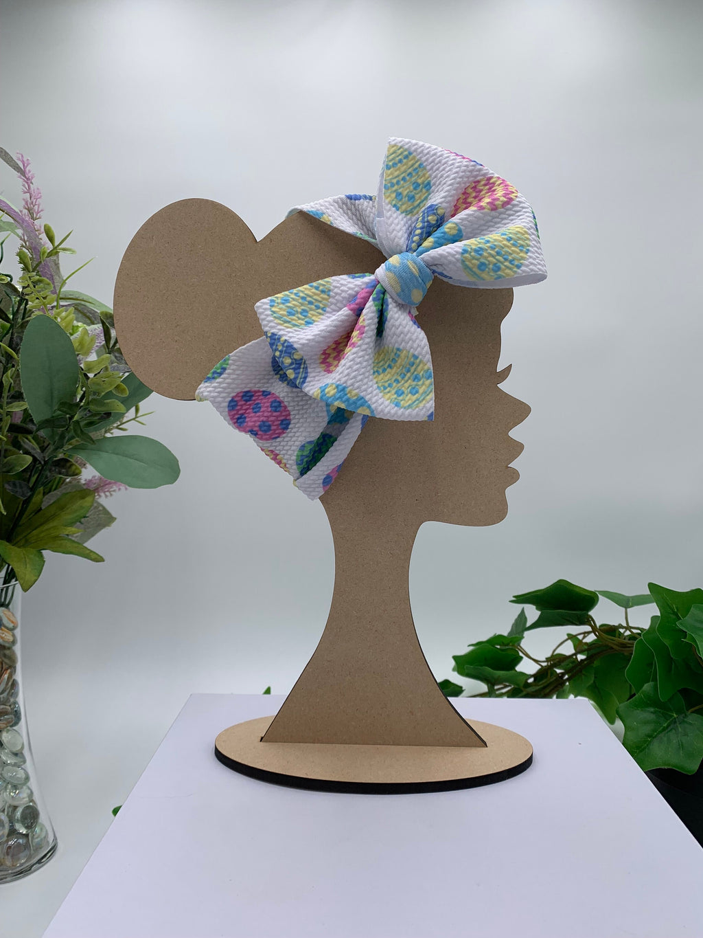 White Headband with a decorative easter eggs themed big bow on a mannequin head silhouette against a white background