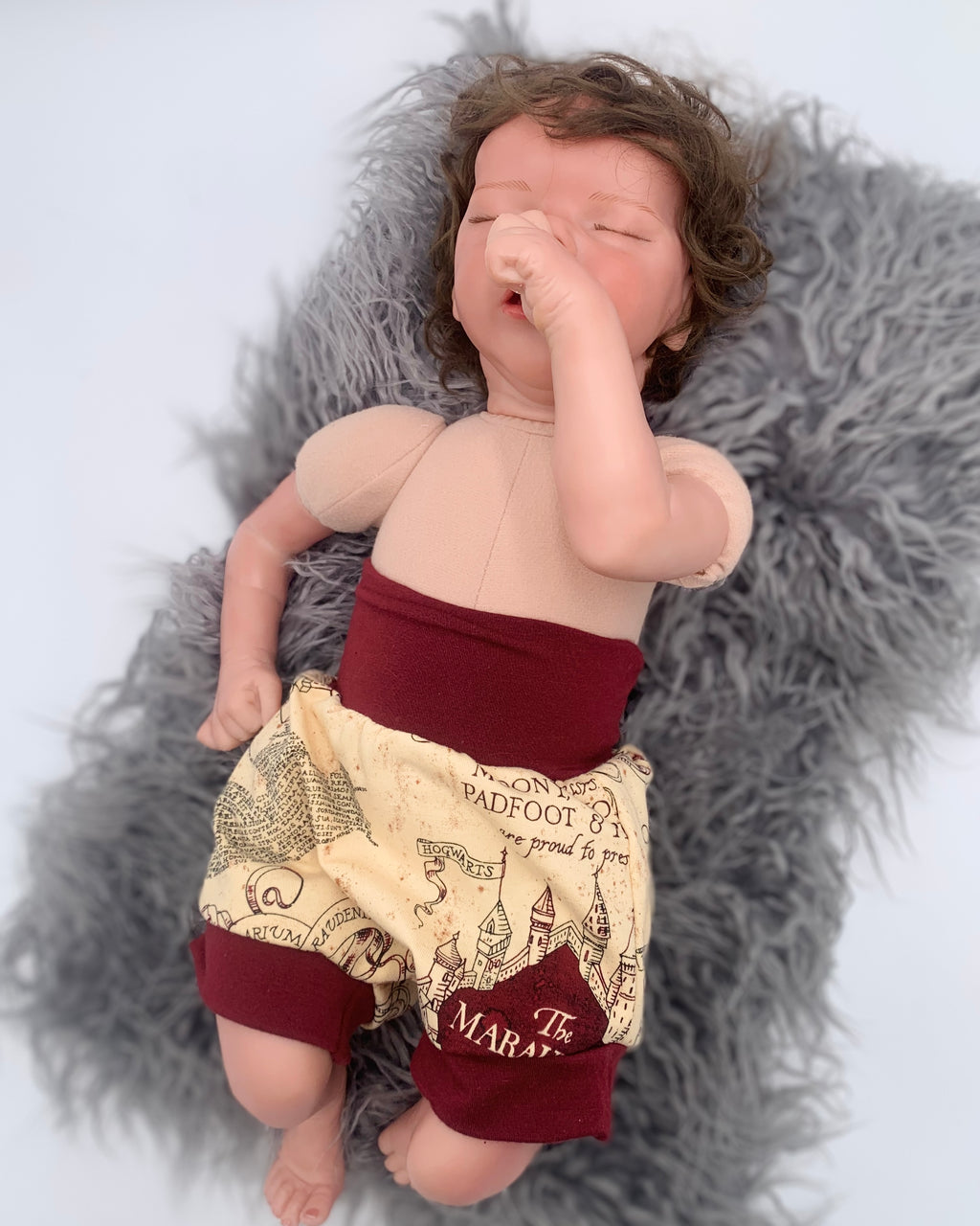 baby doll wearing a beige patterned bloomer with maroon waistband on a white background on a gray fur rug