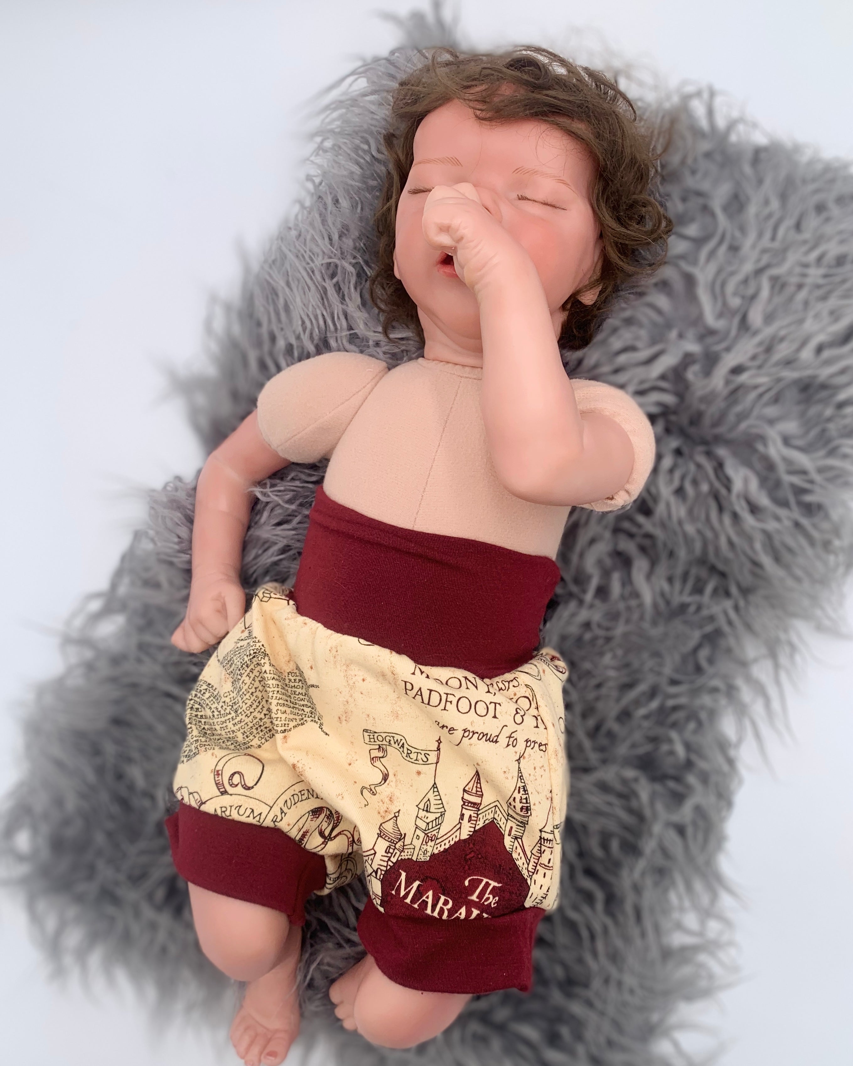 baby doll wearing a beige patterned bloomer with maroon waistband on a white background on a gray fur rug