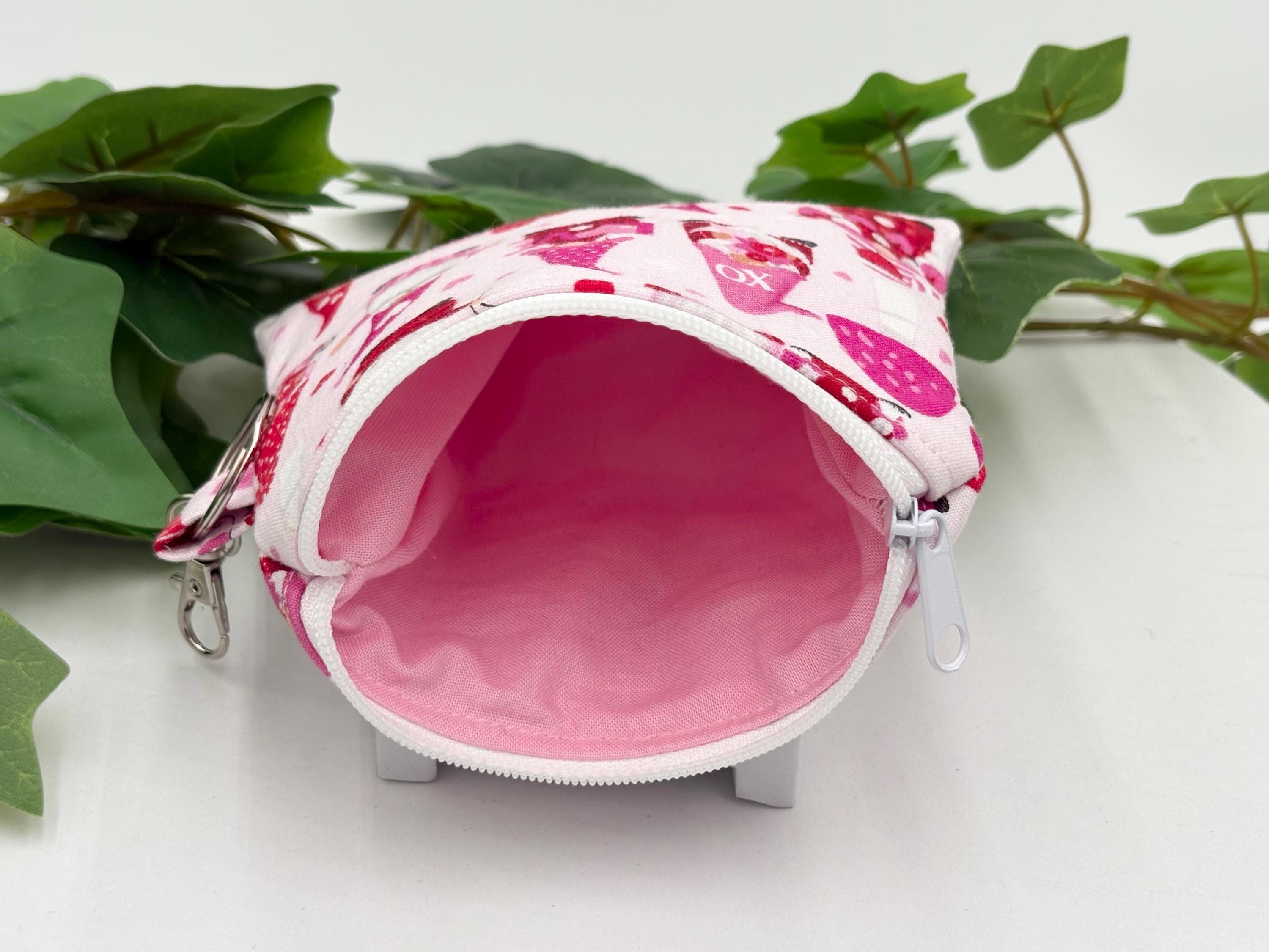 Small coin purse keychain with Valentine-themed gnomes and hearts pattern with zipper opened showing pink lining on a white background with green leaves