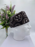 Black KISS band patterned scrub cap on a mannequin head with a white background with flowers