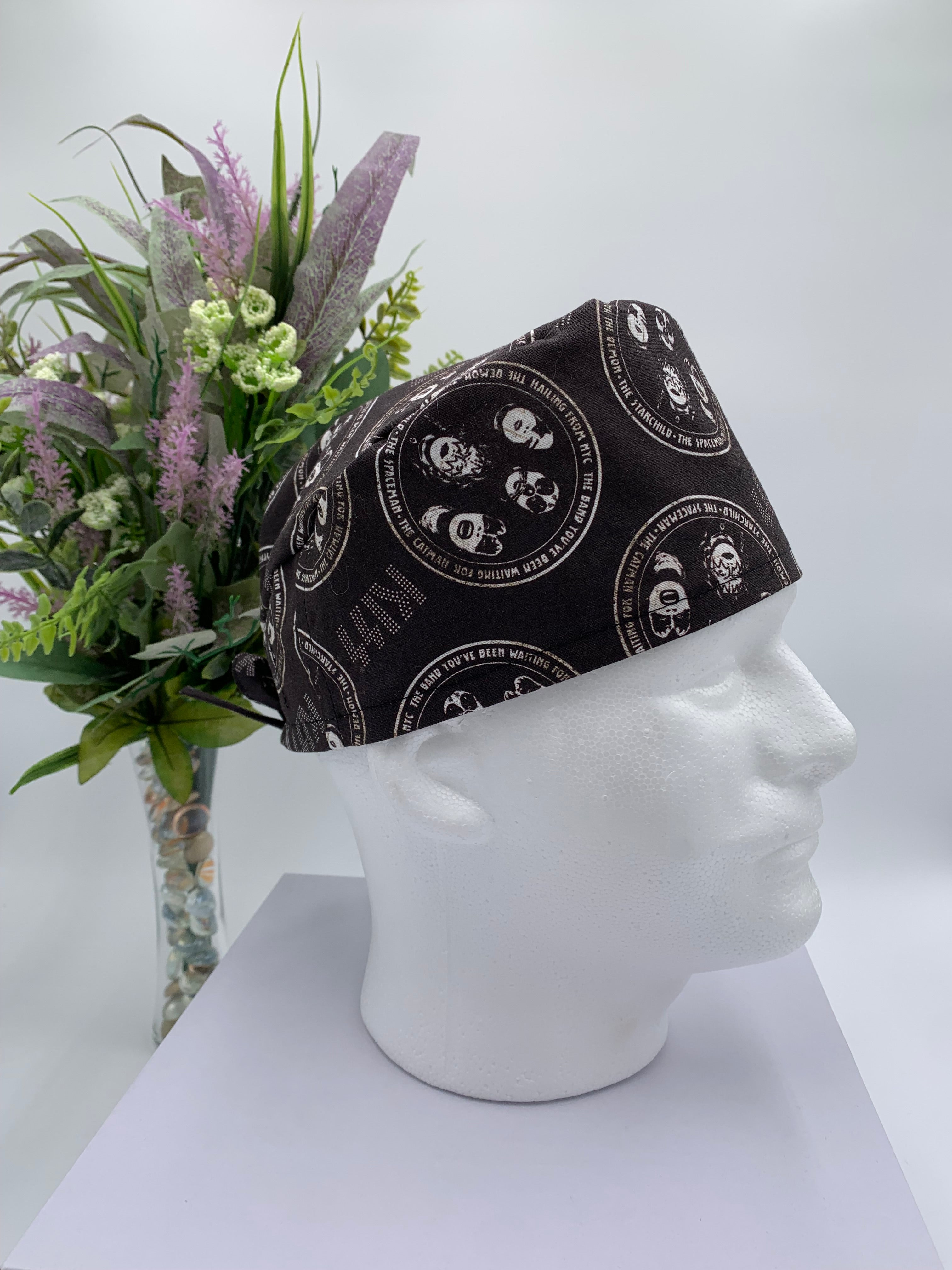 Black KISS band patterned scrub cap on a mannequin head with a white background with flowers
