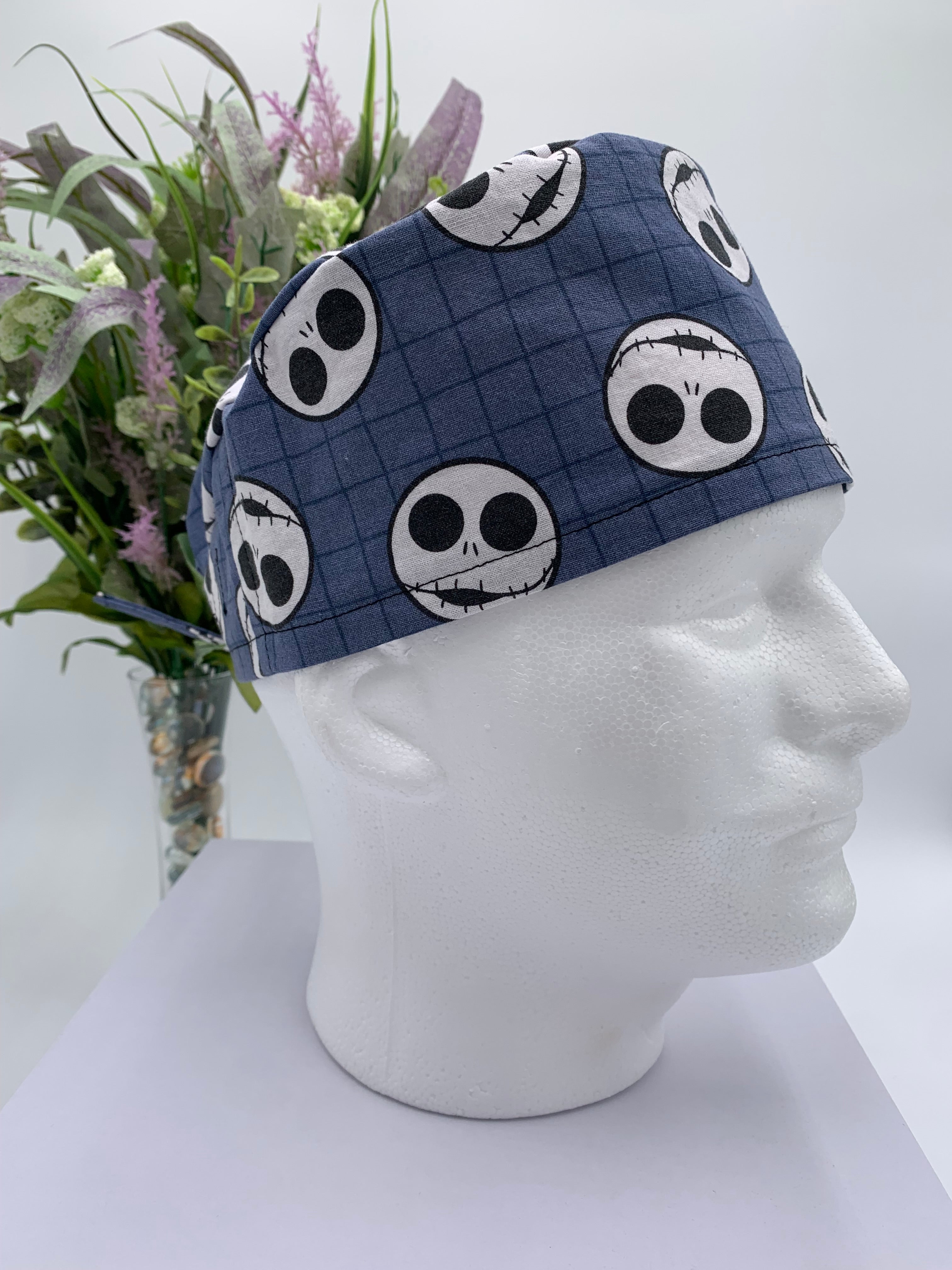 Mannequin head wearing a jack skellington scrub cap with a decorative plant in the background.