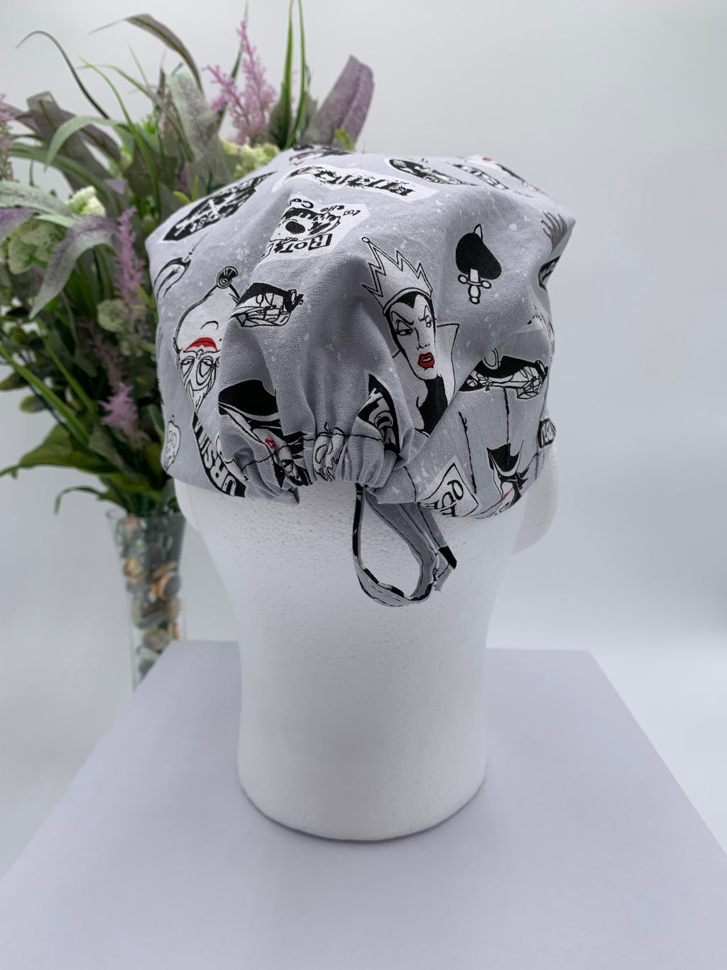 Gray scrub cap with black graphics on a mannequin head against a white background with flowers in the background