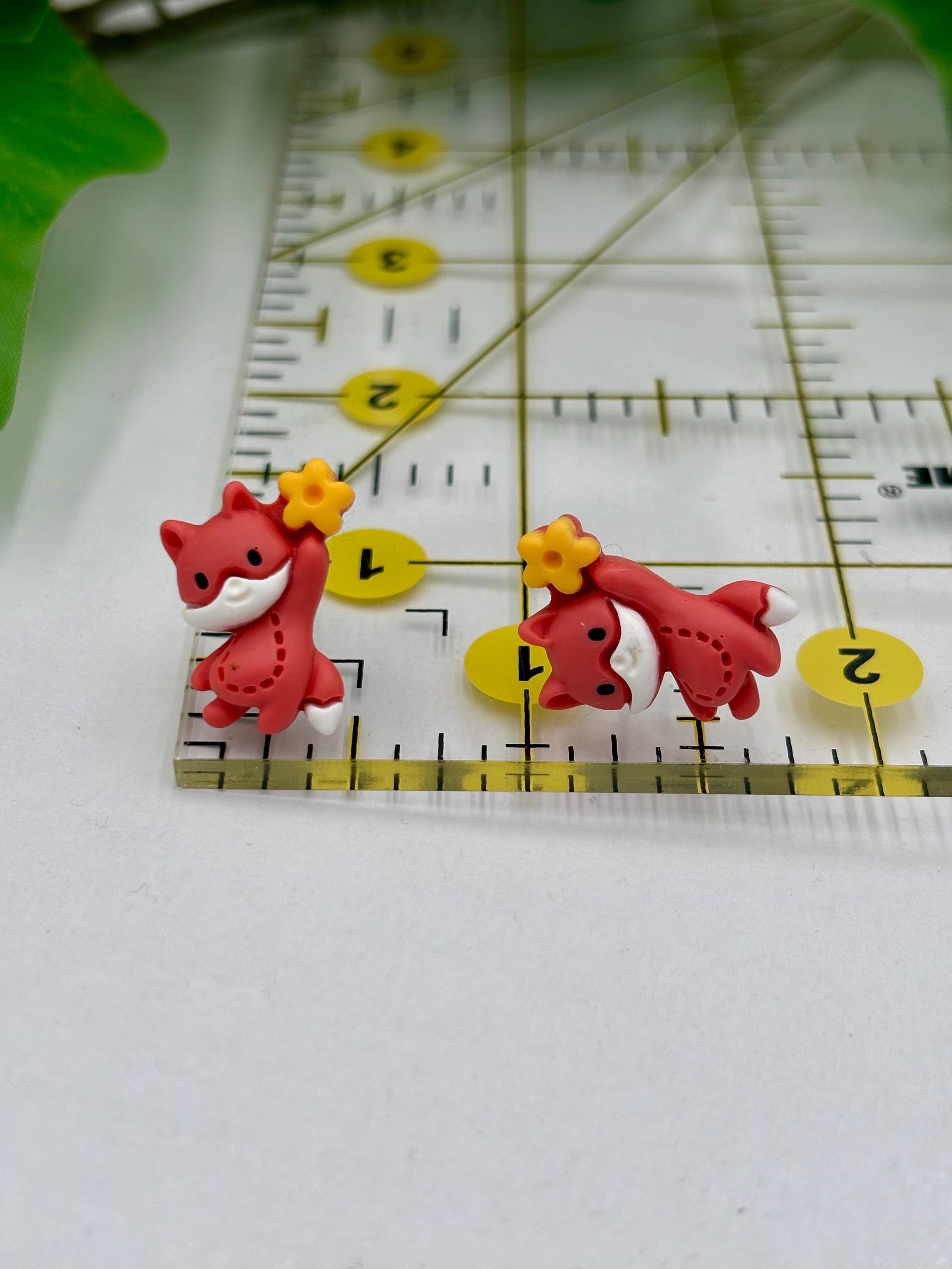 Two red Fox-shaped earrings with yellow flowers on a ruler for scale.