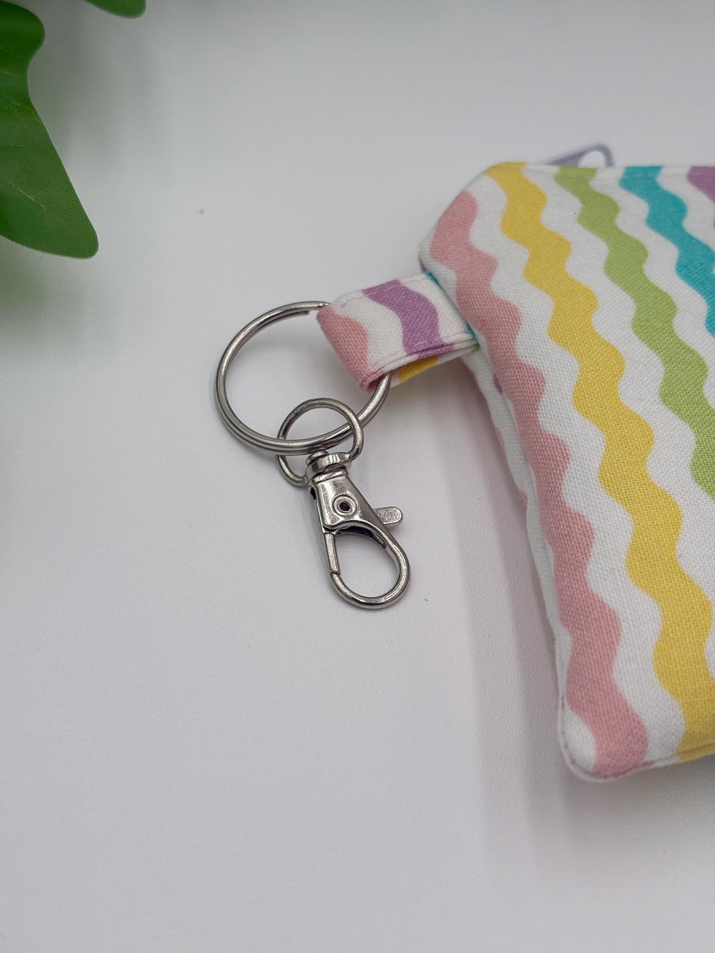 close up of keychain on Small coin purse keychain with pastel zigzag pattern on a white background with green leaves 