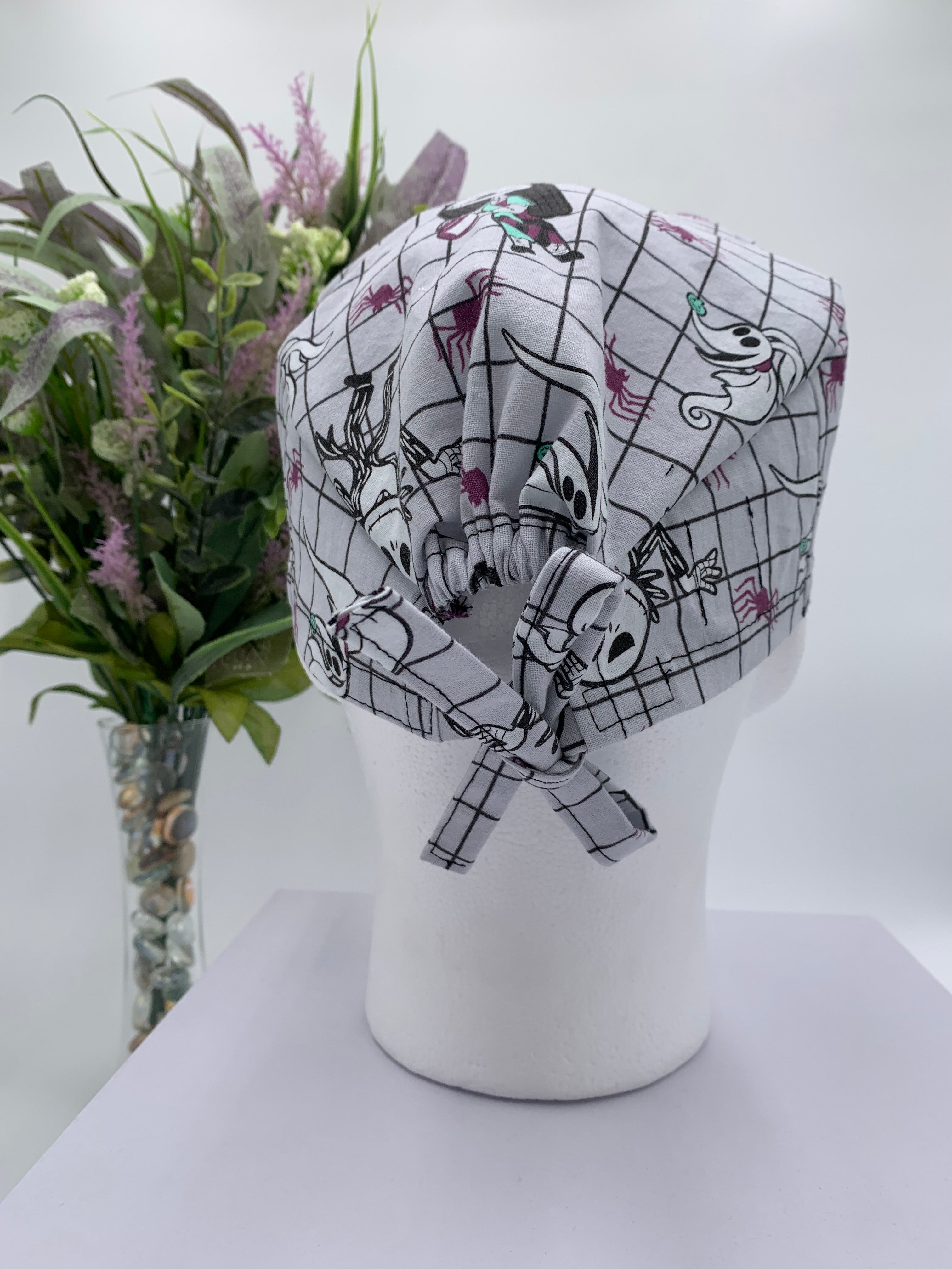 Mannequin head wearing a nightmare before christmas scrub cap with a decorative plant in the background.