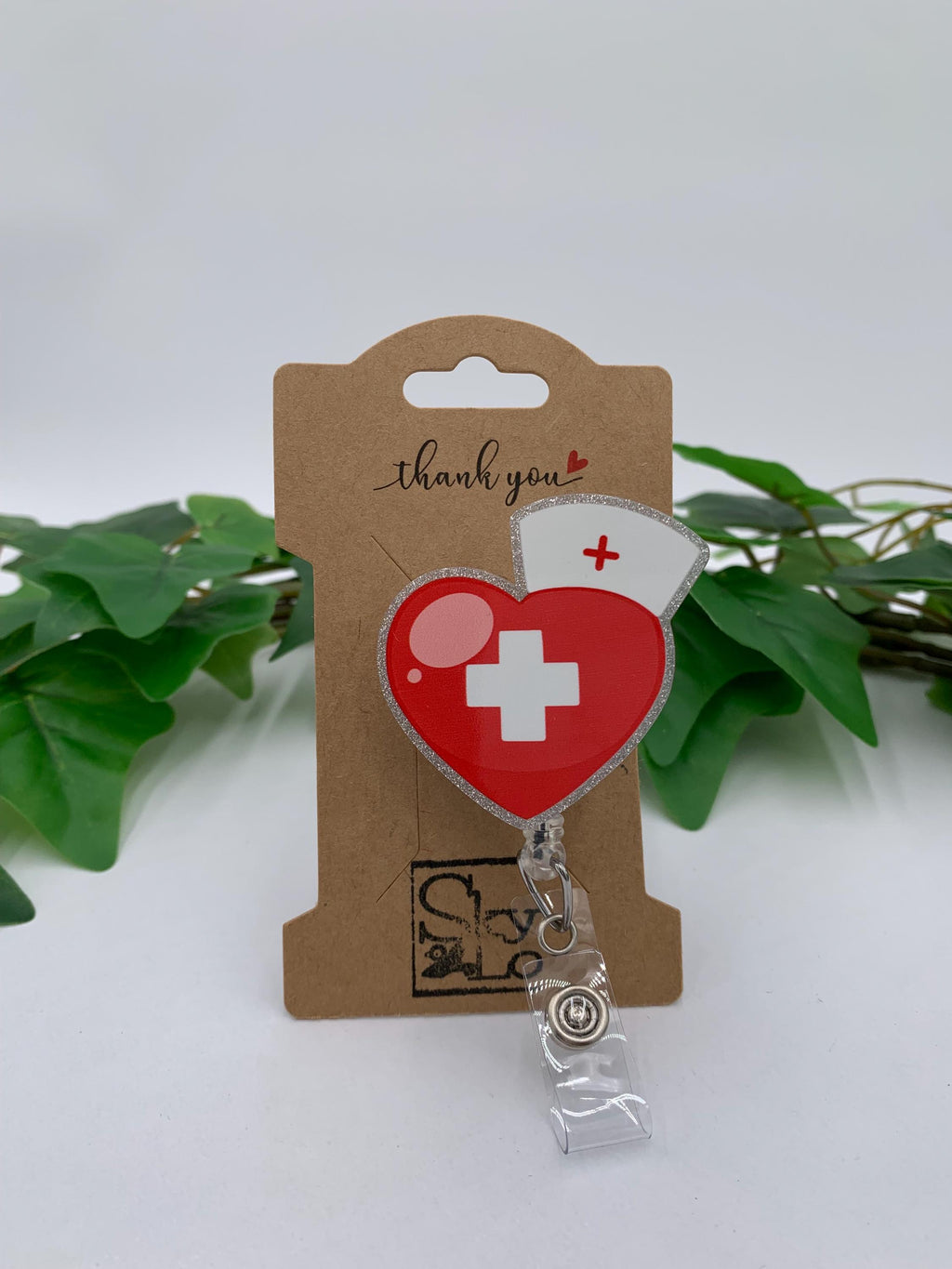 Heart-shaped badge reel with nurse design on a 'thank you' card with green leaves in the background