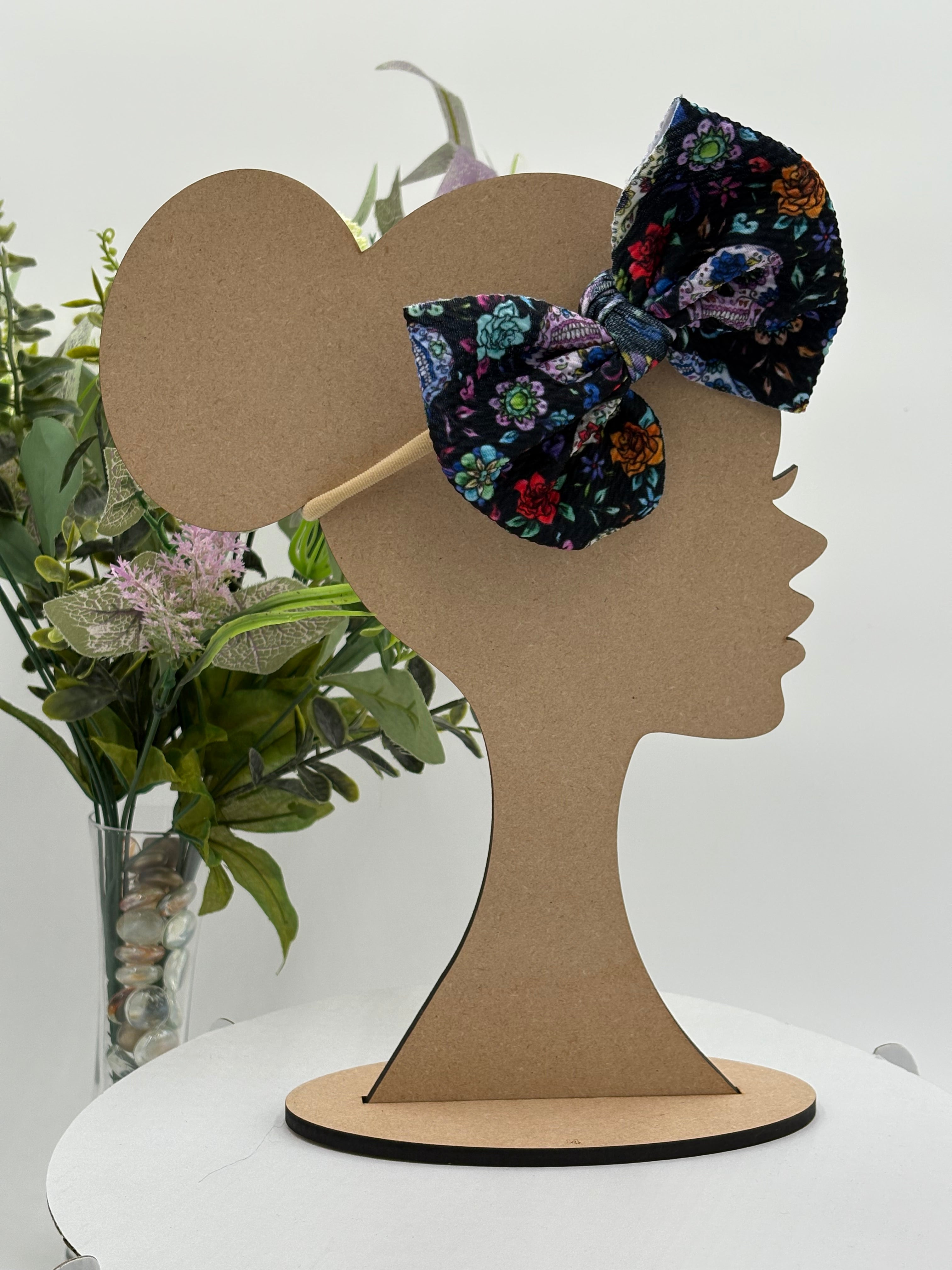 Day of the dead sugar skulls themed big bow nylon headband on a mannequin head with a white background and greenery 