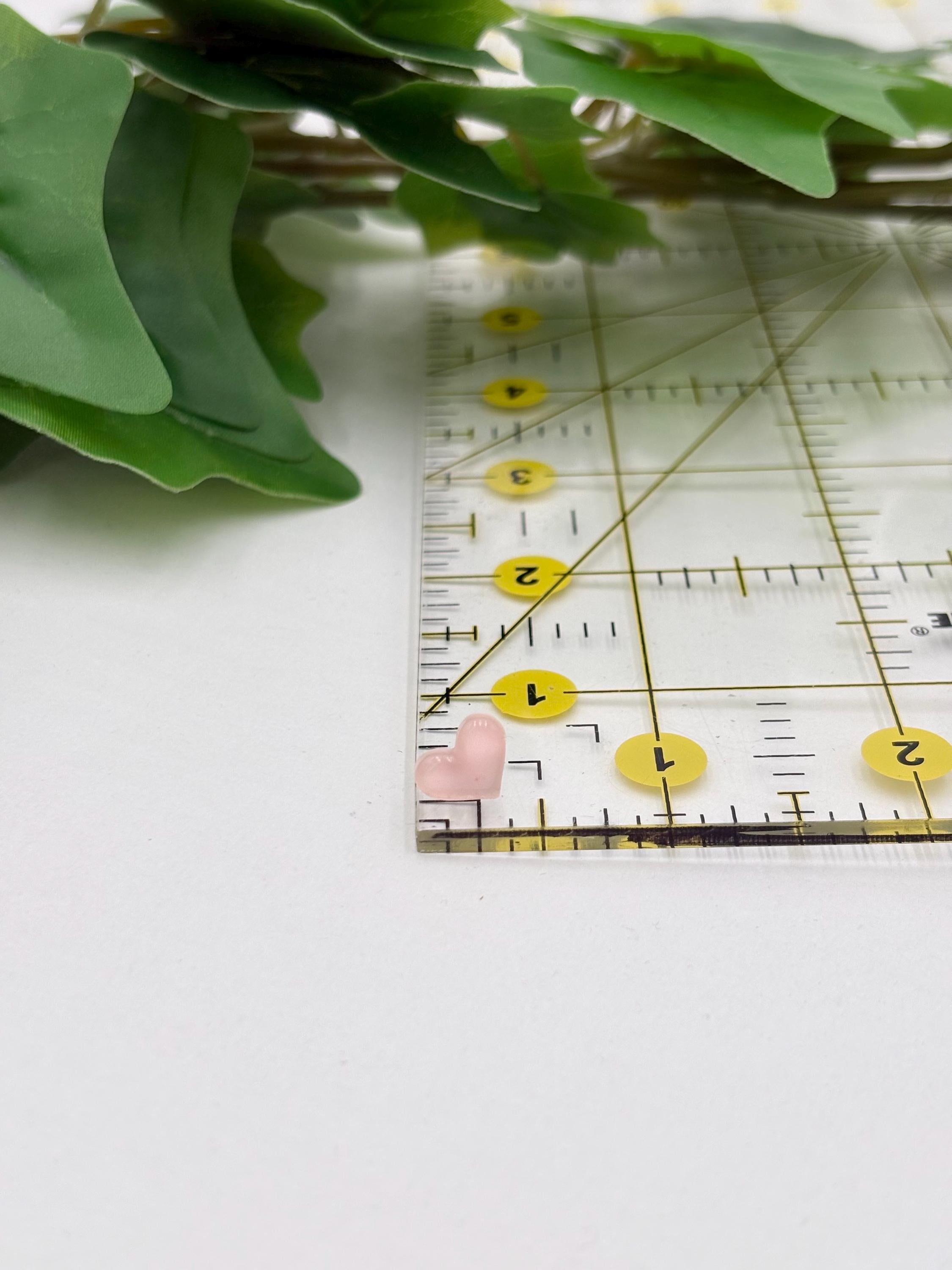Pink heart shaped earring on a Ruler on a white surface with green leaves in the background