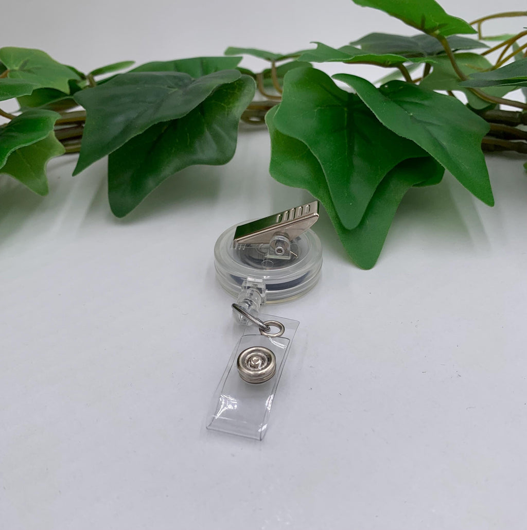 Clear badge holder with a clip on a white surface with green leaves in the background