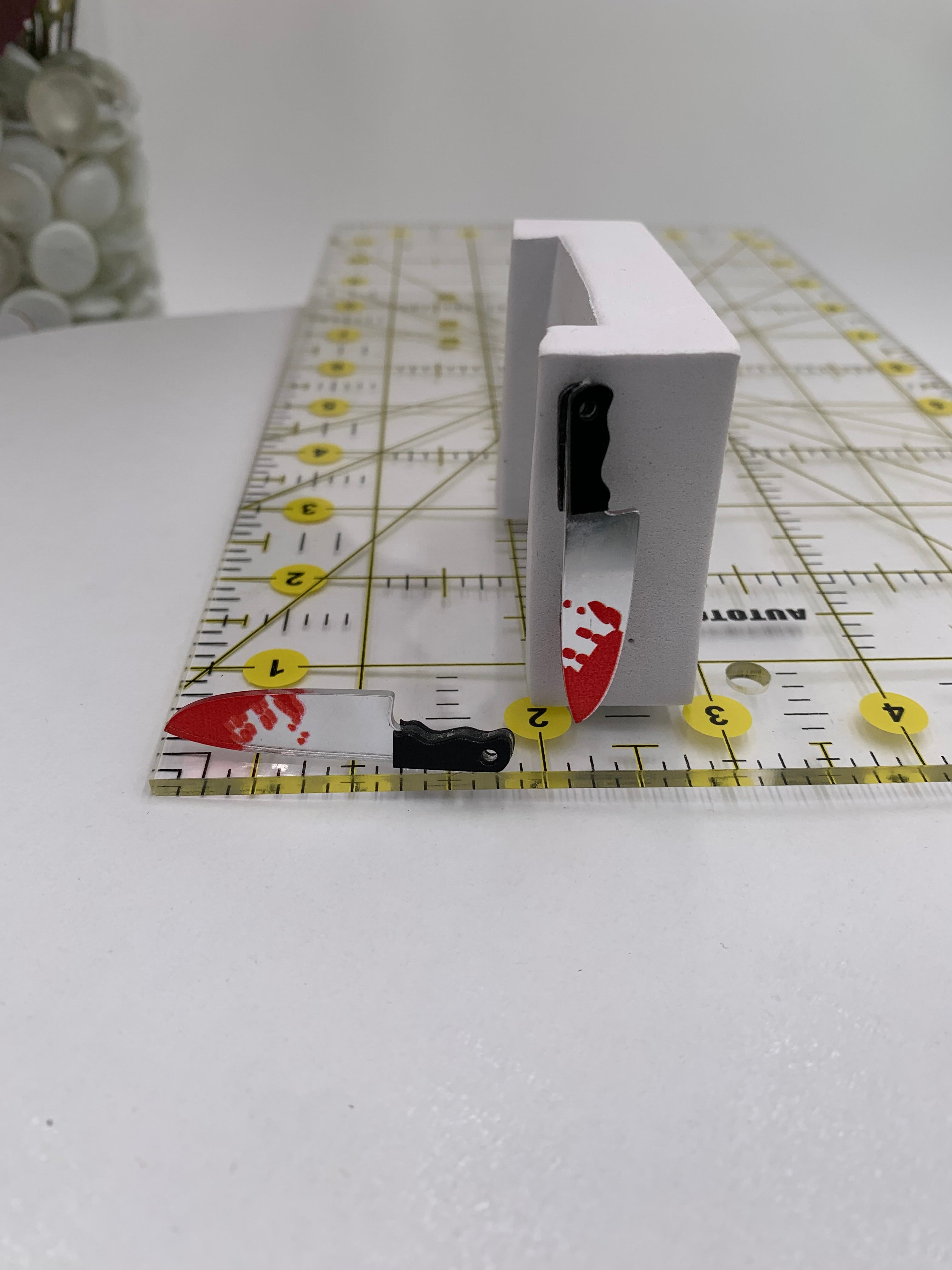 Bloody butcher knife earring next to a ruler with measurement markings at 2 inches and 1/2 inch