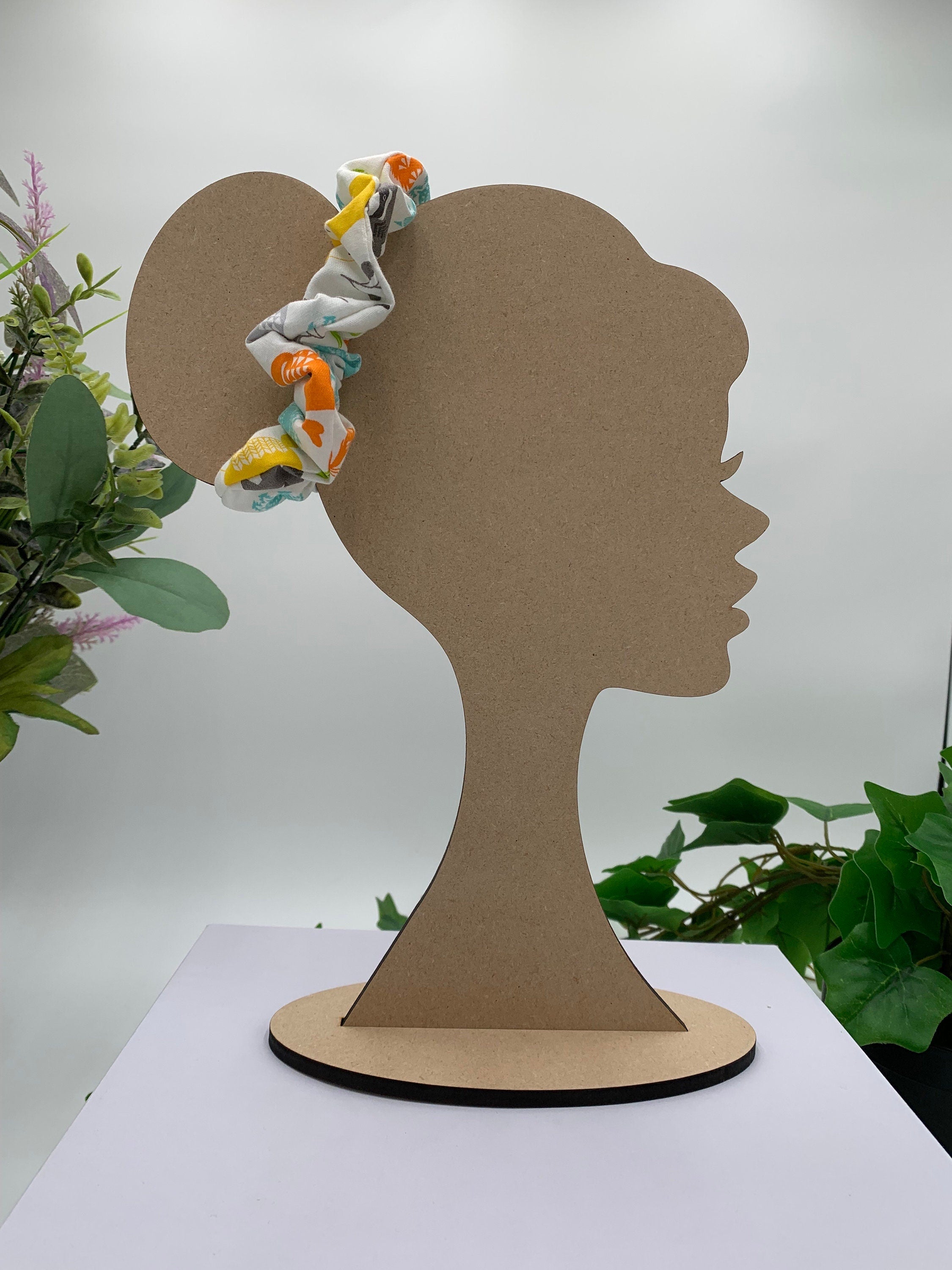 White with patterned colored woodland critters scrunchie on a cardboard silhouette of a head with plants in the background
