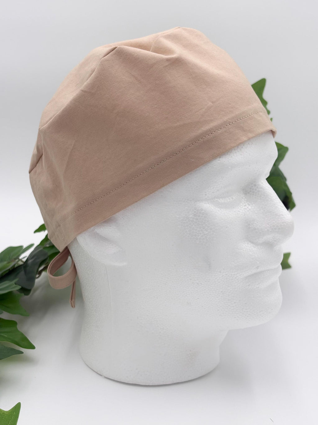 Beige scrub cap on a mannequin head with a white background