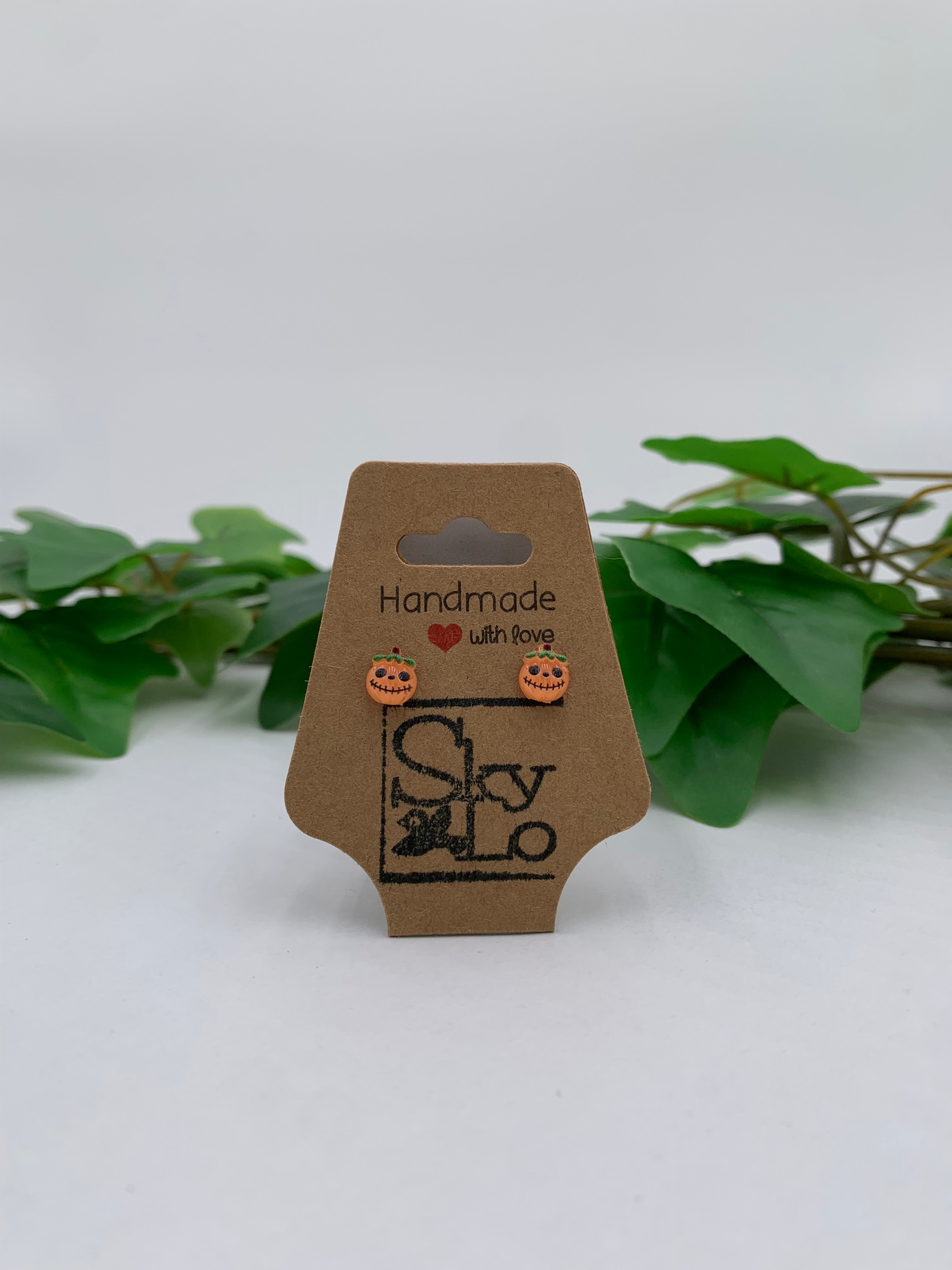 Pair of Jack-O-Lantern earrings on a 'Handmade with Love' branded card with green leaves in the background