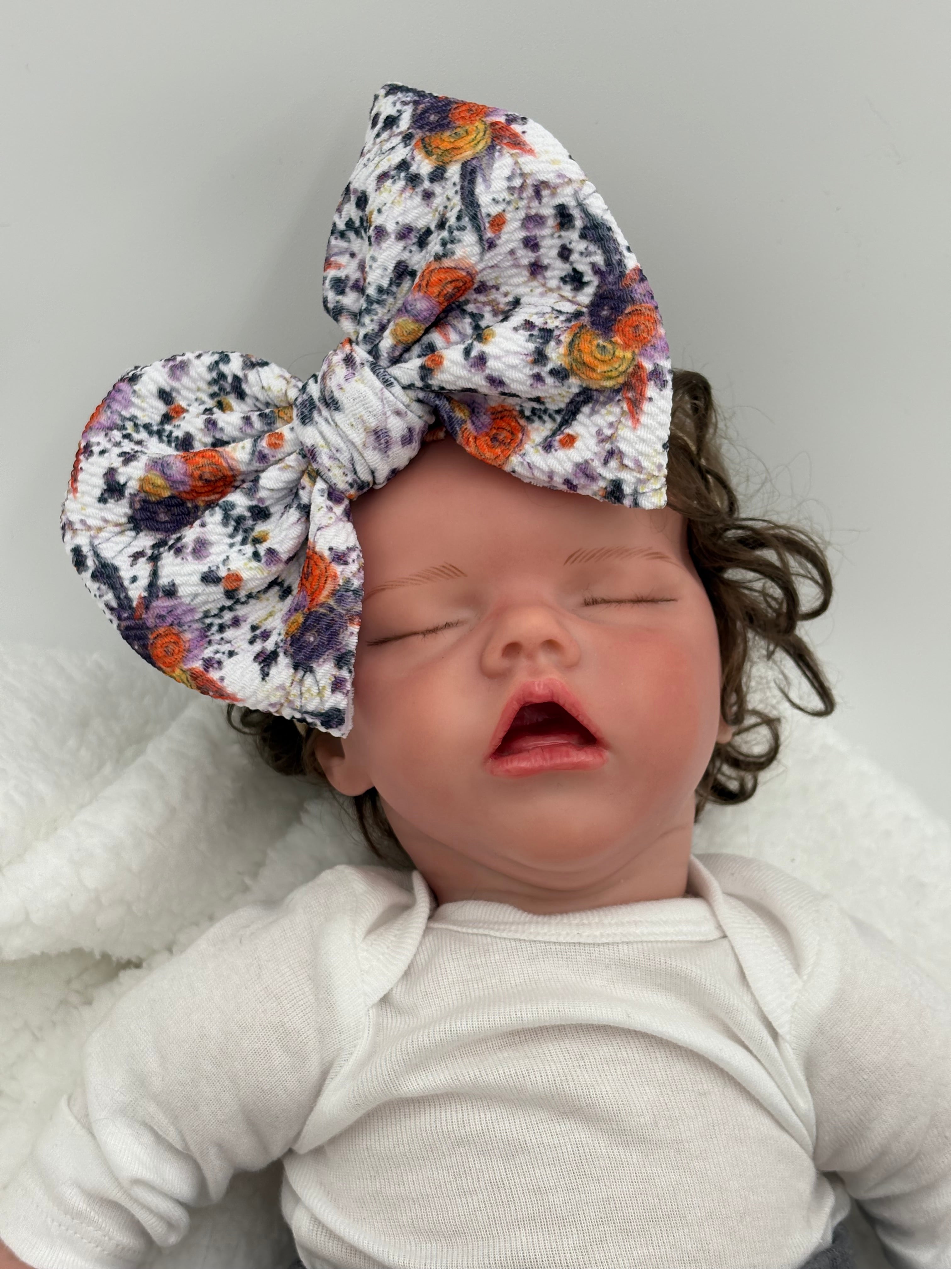 baby doll wearing a Autumn floral themed big bow nylon headband on a white background