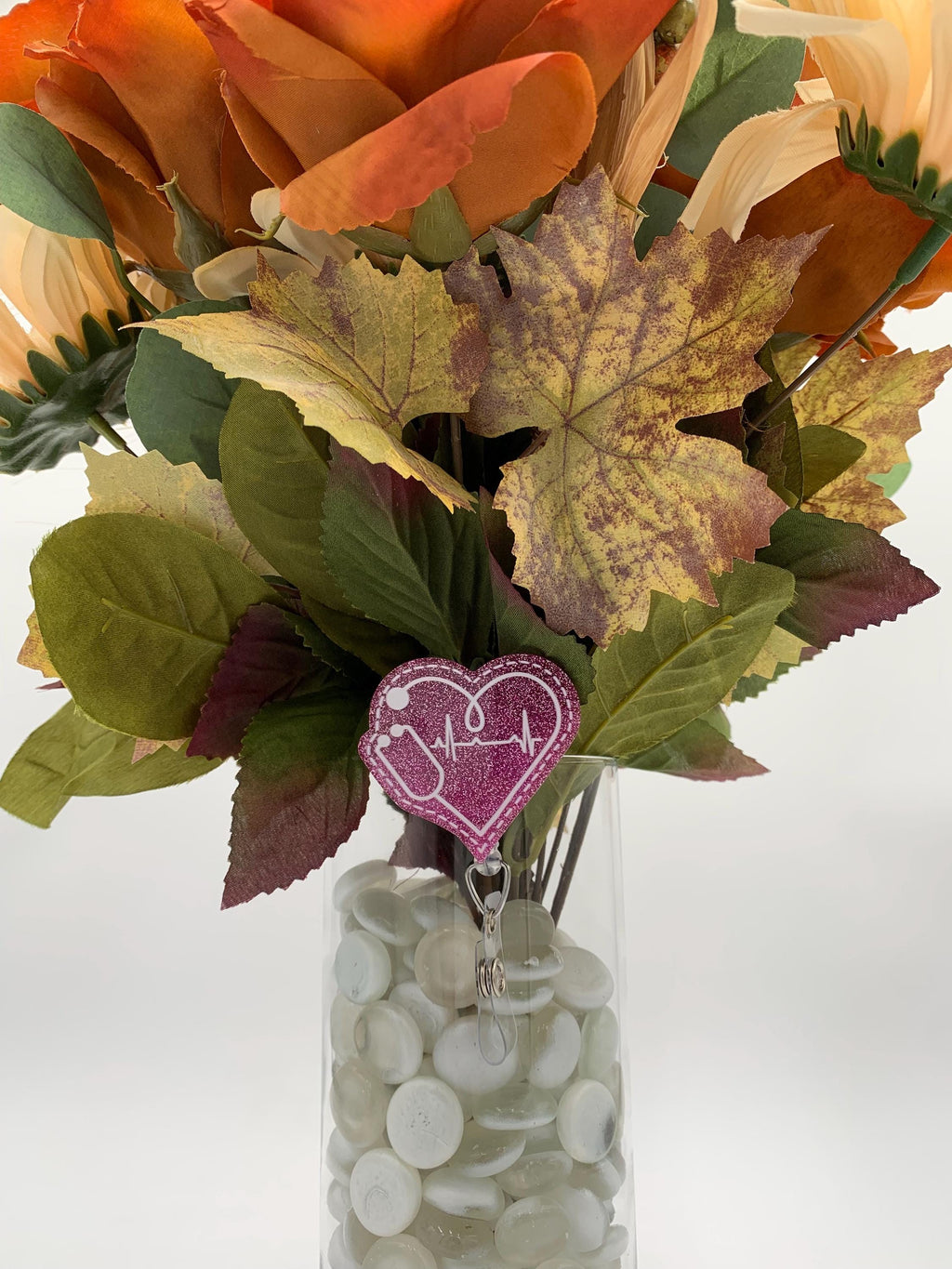 Bouquet of autumn leaves with a pink heart-shaped badge reel in a clear vase on a white background
