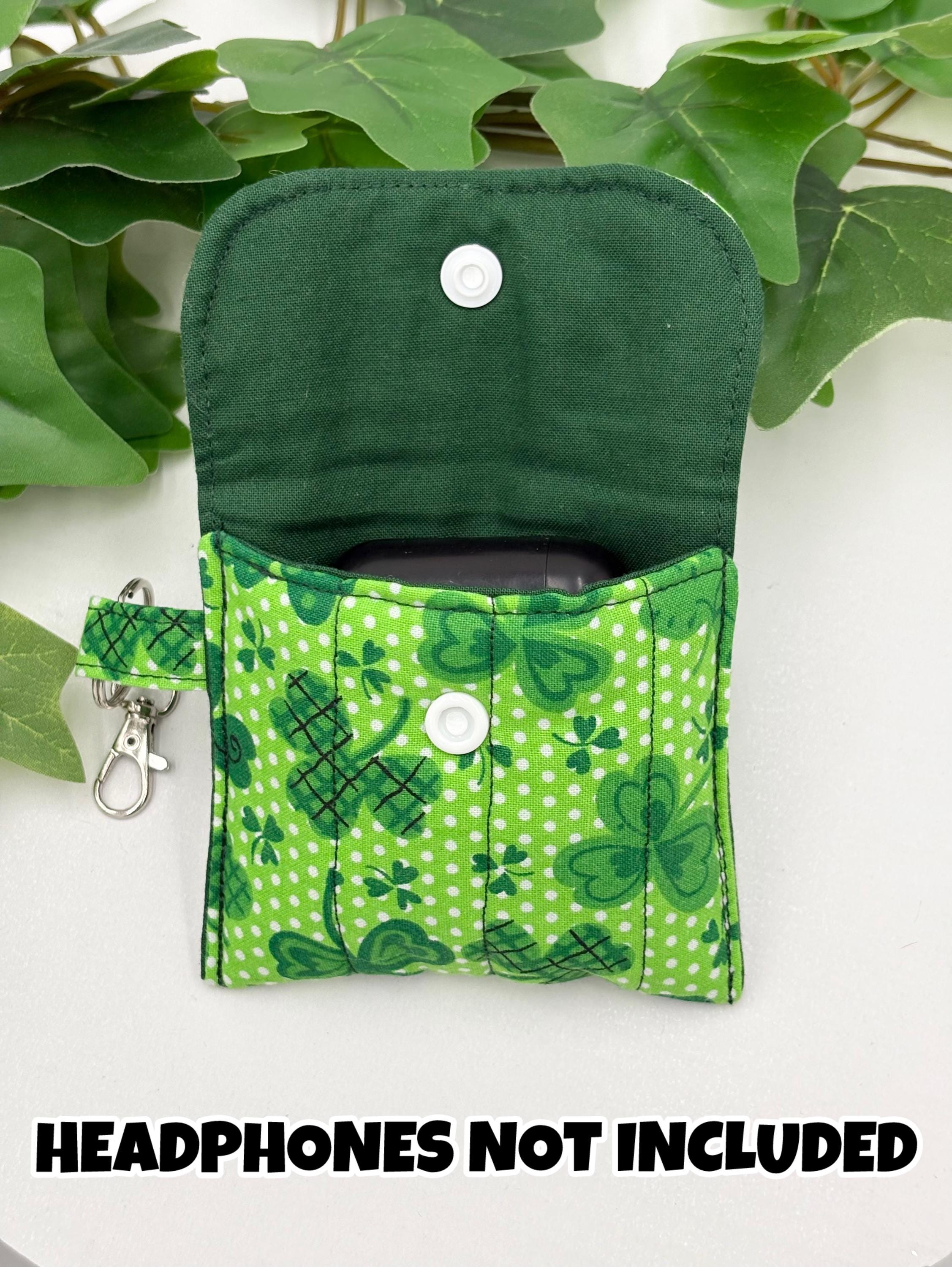 Opened Small quilted headphone holder pouch keychain with green shamrocks design showing a green liner with black headphone case inside on a white surface with green leaves with text "Headphones not included"