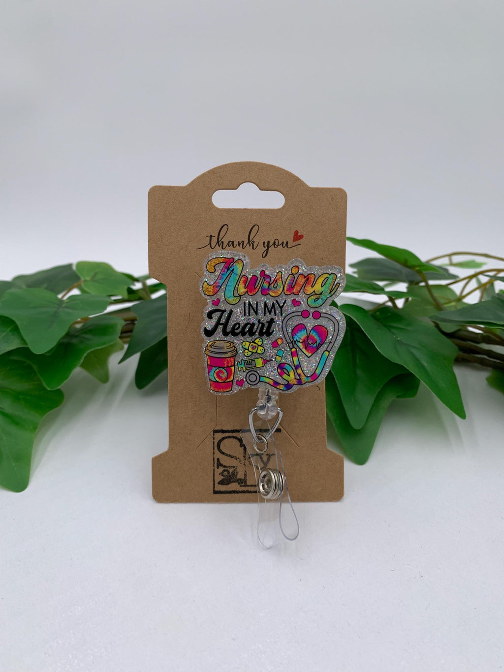 Retractable badge holder with colorful design on a brown card, surrounded by green leaves.