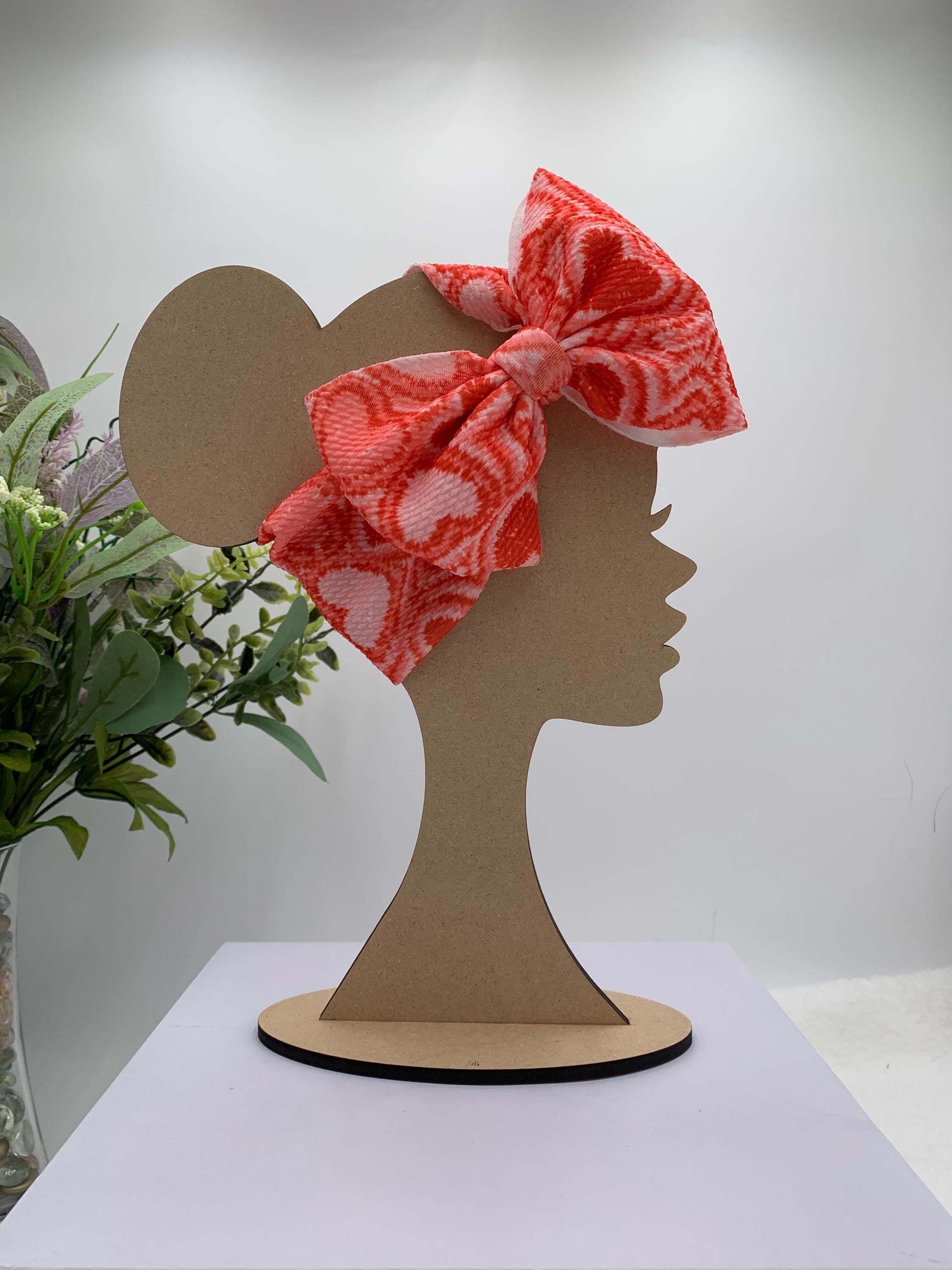 Red and Pink Headband with a decorative hearts themed big bow on a mannequin head silhouette against a white background