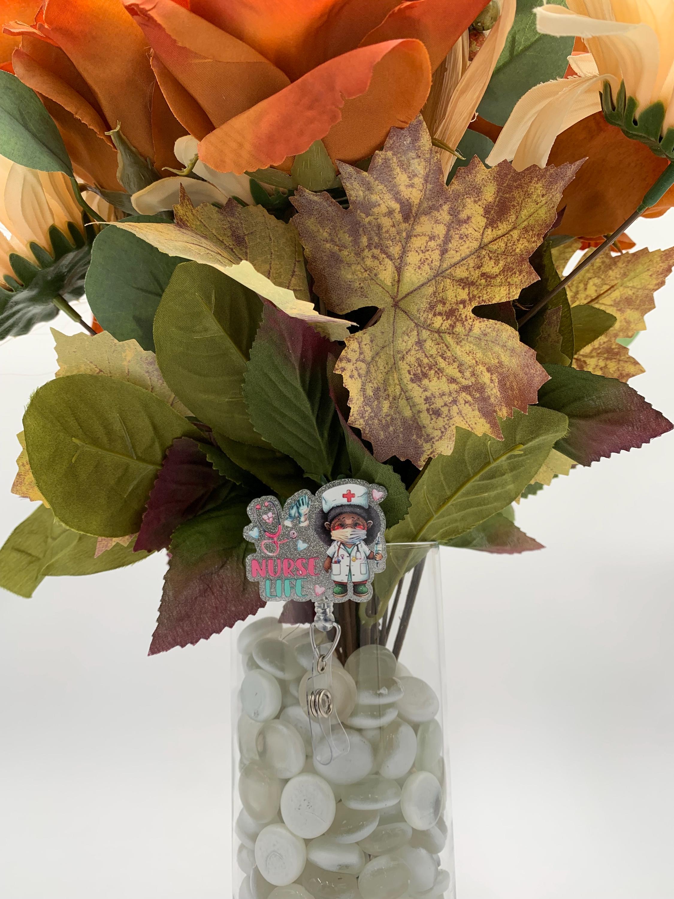 Bouquet of autumn leaves and flowers with a clear vase containing a badge reel that says "Nurse Life"