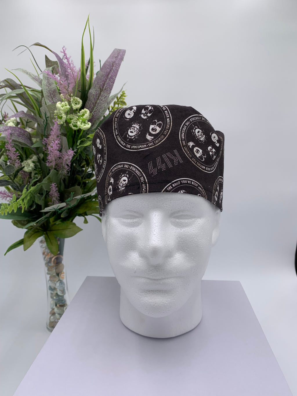 Black KISS band patterned scrub cap on a mannequin head with a white background with flowers