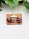 Pair of dark brown faux fur leopard print earrings on a cardboard backing with a plant in the background.