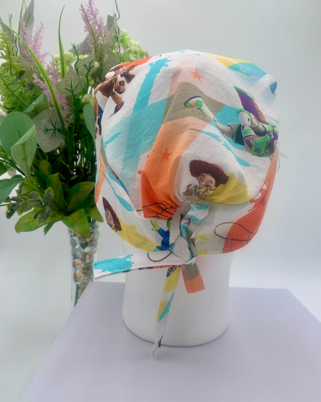 Colorful Toy Story scrub cap on a mannequin head with flowers, against a white background