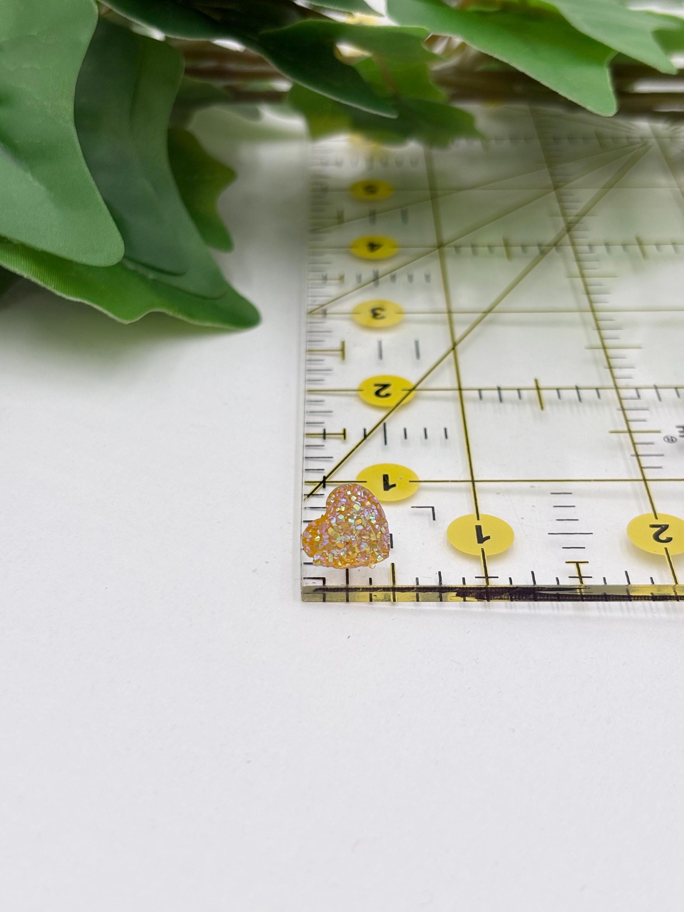 Ruler with yellow sparkling heart shaped earring on a white surface with green leaves in the background