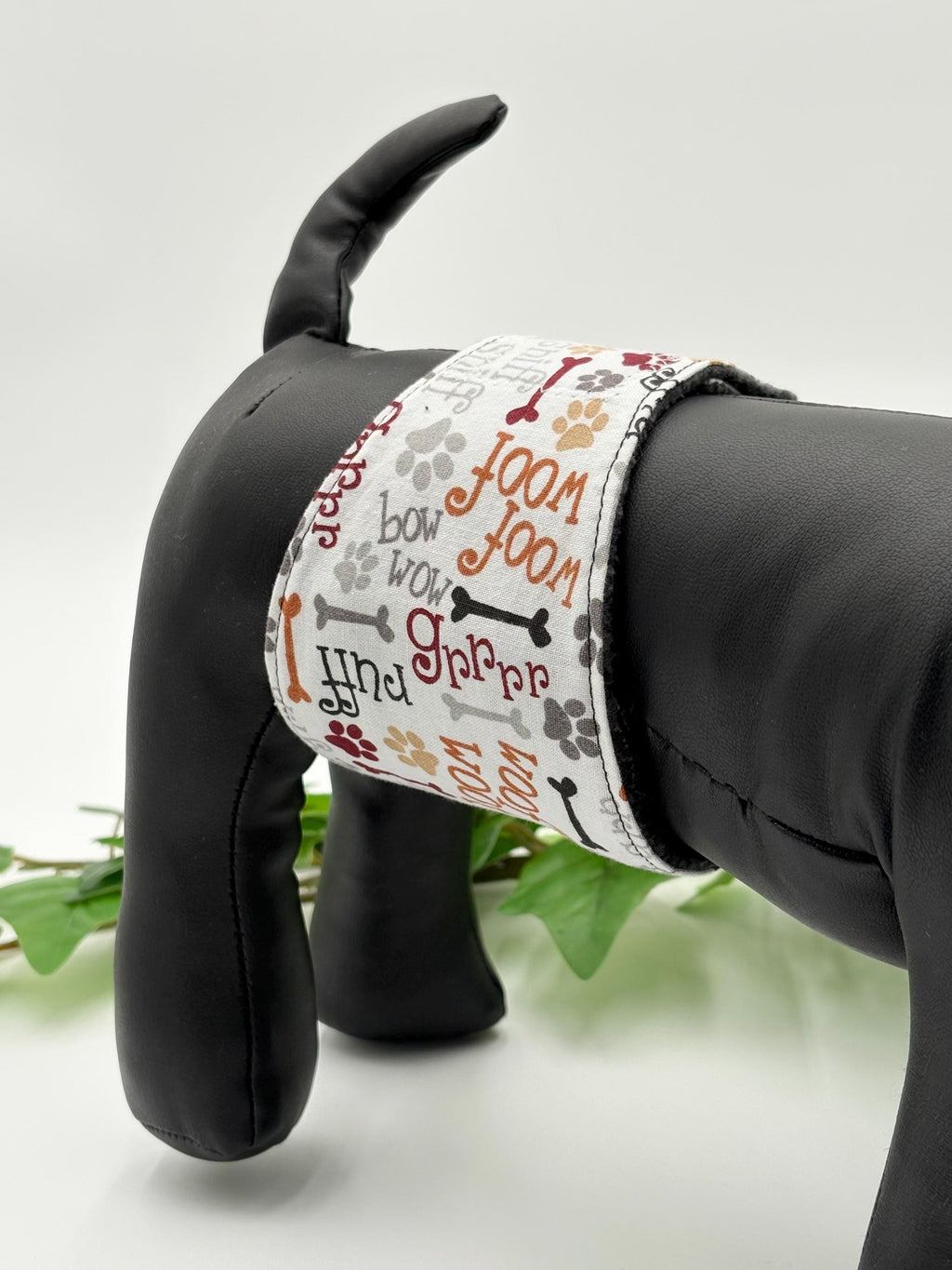 The dog belly band with wood and grr material with the incontinence pad in it on a black dog mannequin with a plant and white background 