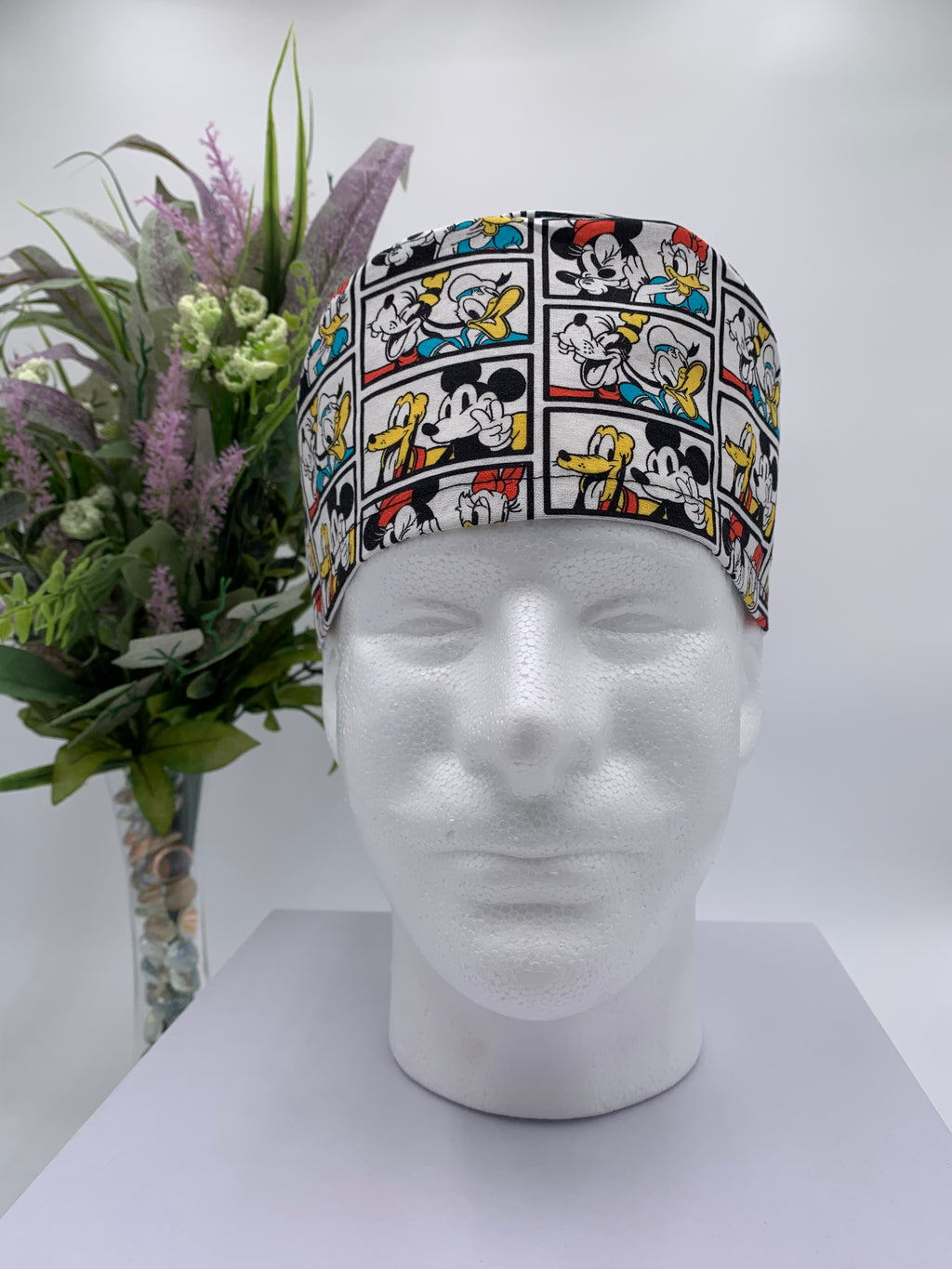 Mickey Mouse scrub cap on a mannequin head with a white background and flowers in the background