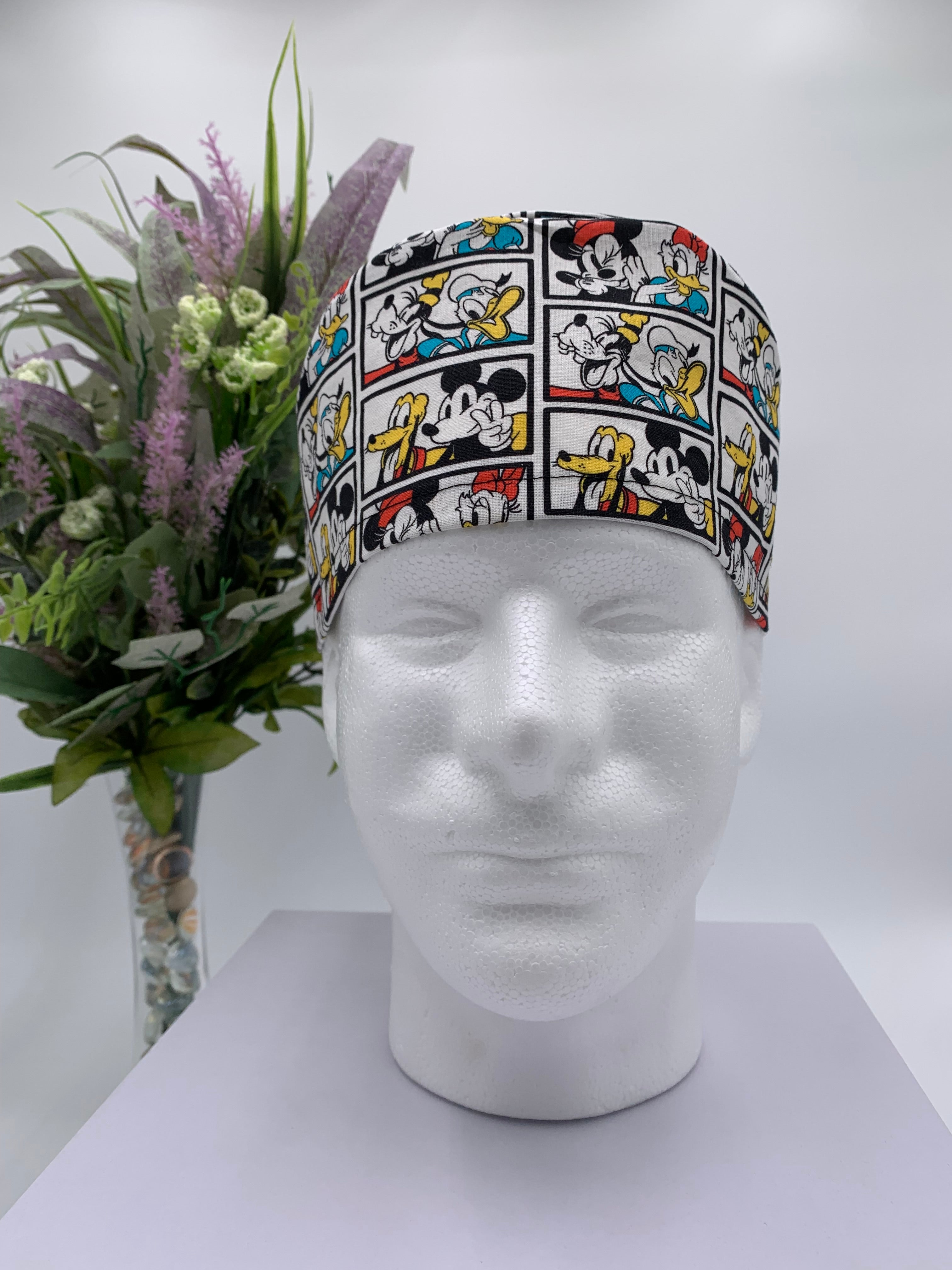 Mickey Mouse scrub cap on a mannequin head with a white background and flowers in the background