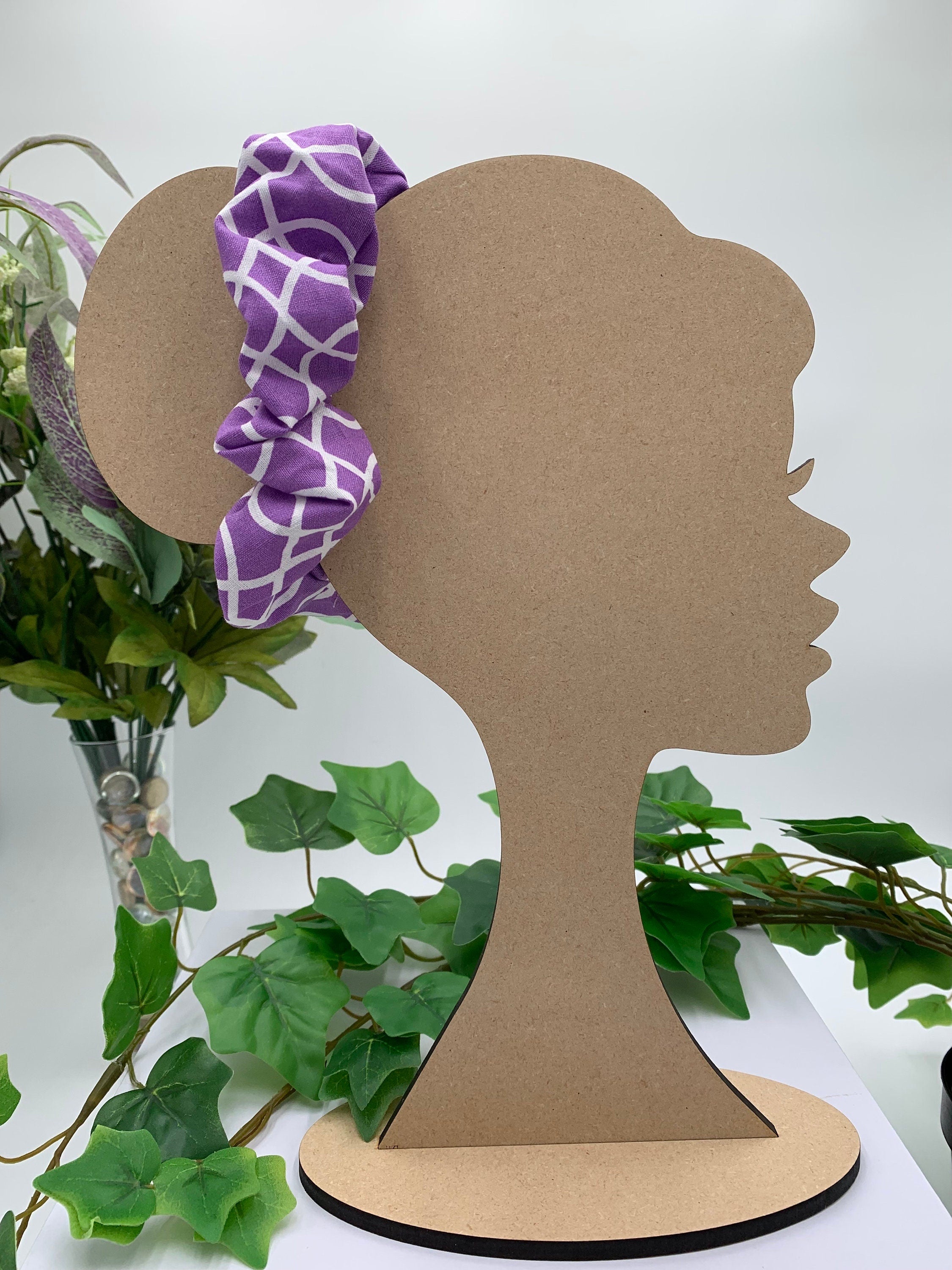 Purple and white geometric print scrunchie on a cardboard silhouette of a head with plants in the background