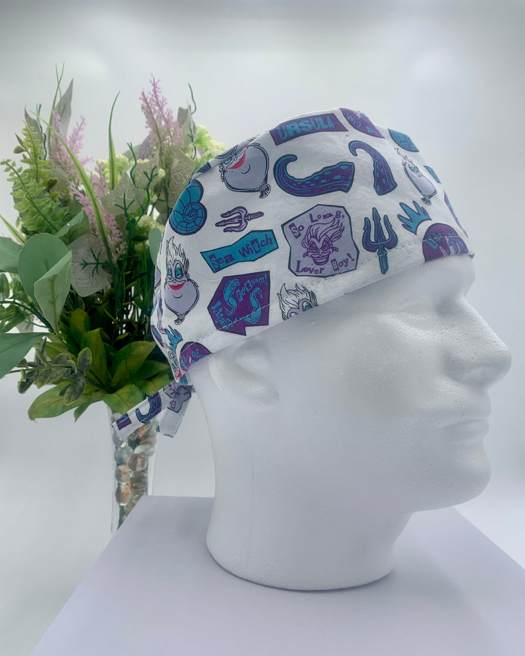 Colorful Little Mermaid Ursula scrub cap on a mannequin head with flowers, against a white background