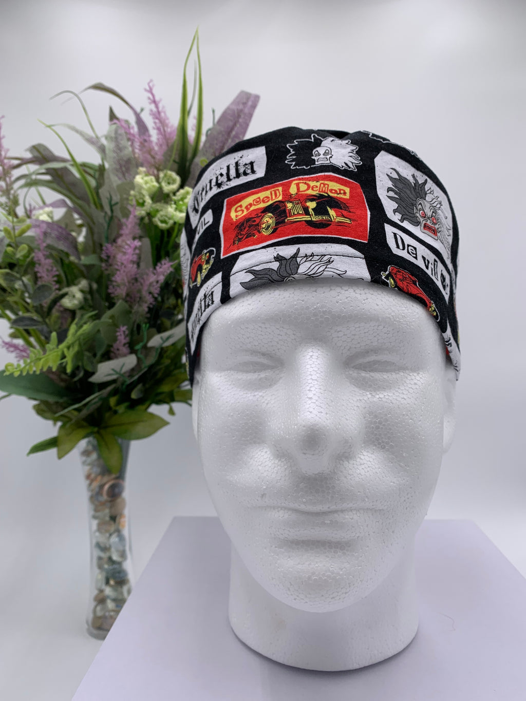 Mannequin head wearing a Cruella DeVil scrub cap with a decorative plant in the background.