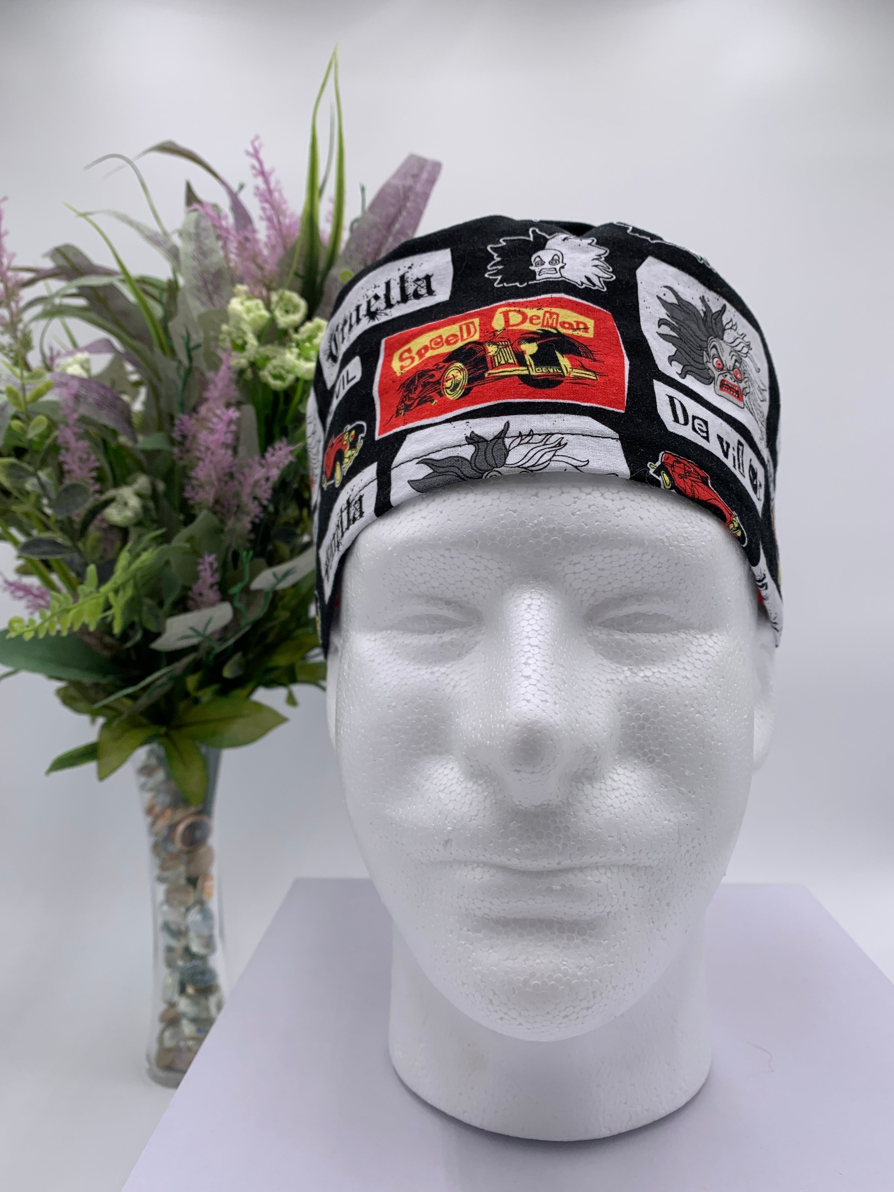 Mannequin head wearing a Cruella DeVil scrub cap with a decorative plant in the background.